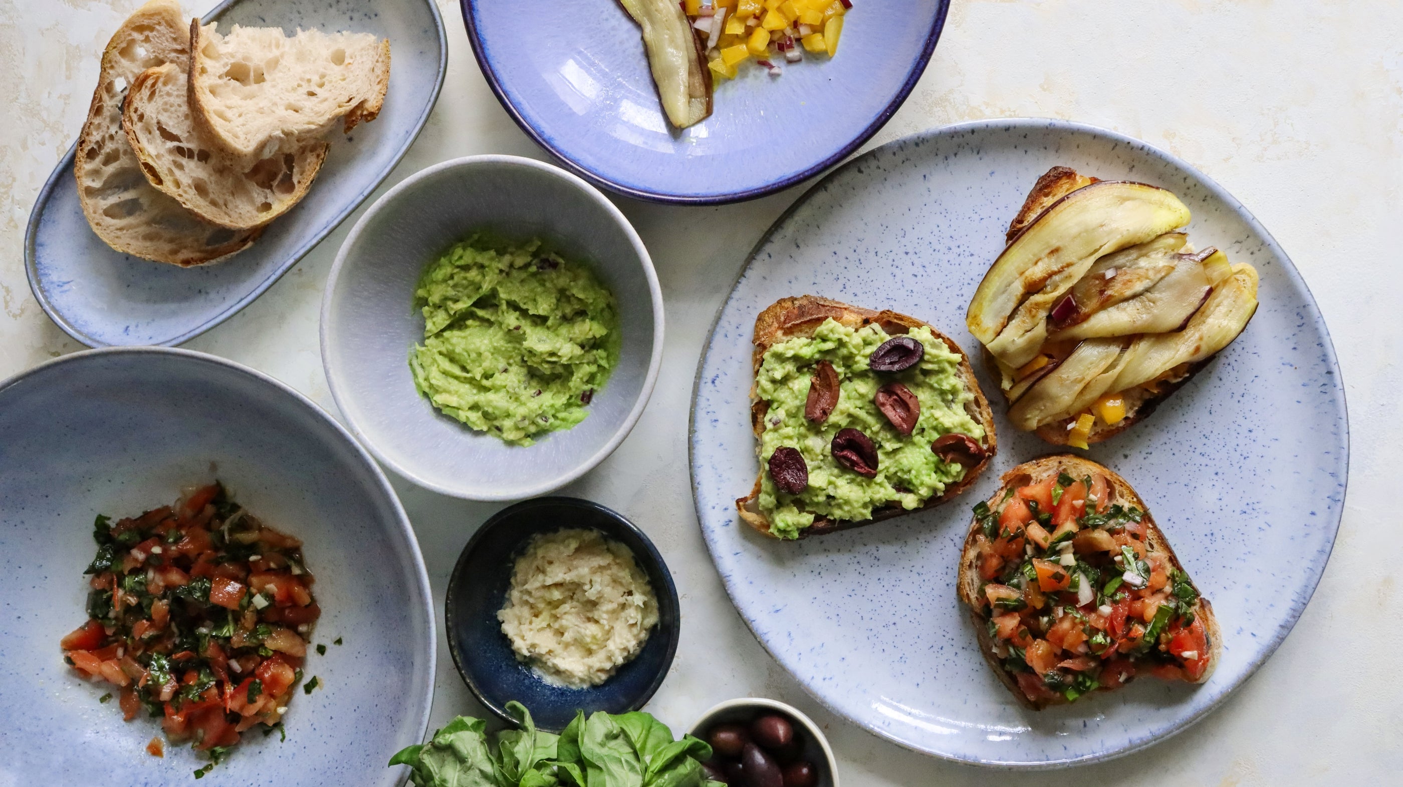 Verschiedene belegte Brotscheiben mit Avocado, Tomaten und Gemüse auf Tellern, umgeben von Schüsseln mit Dips.