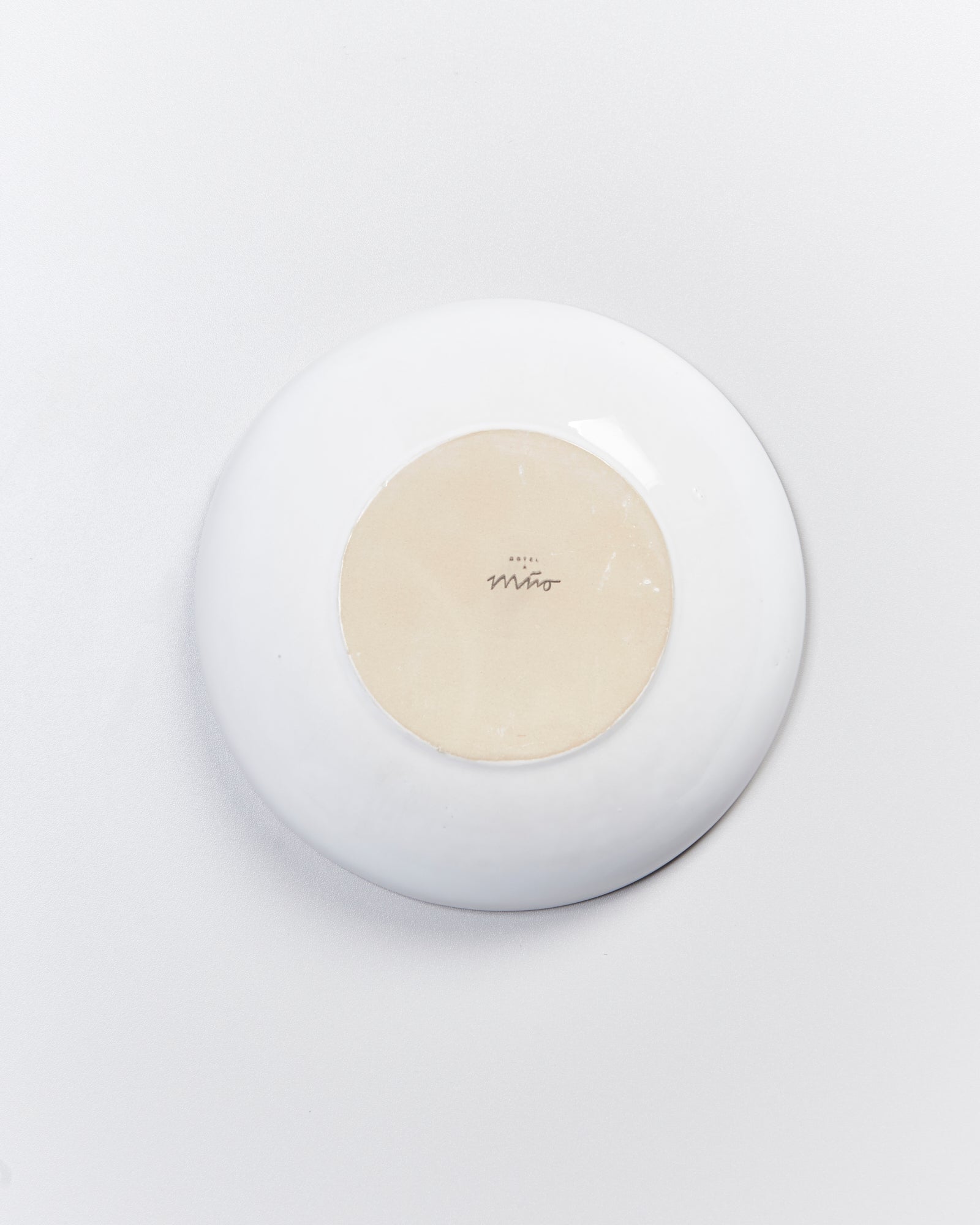 Unterseite eines weißen Tellers mit einem sandfarbenen Kreis und einem Schriftzug in der Mitte.