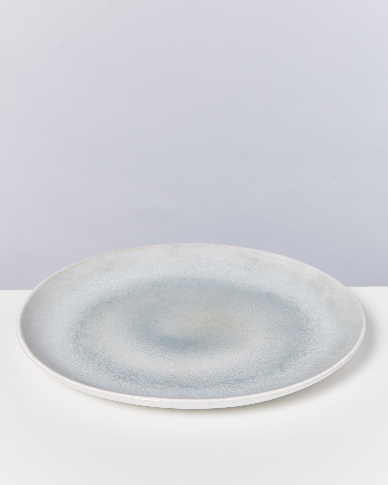 Grauer, runder Keramikteller mit subtilen Verfärbungen auf einem weißen Hintergrund.