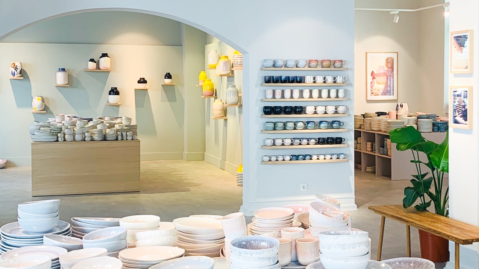 Heller Raum mit Regalen voller Töpferwaren und einem Tisch, der mit gestapelten Schüsseln und Tellern bedeckt ist.