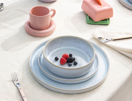 Ein gedeckter Tisch mit grauem Geschirr, Beeren, einer rosa Tasse und einem rosa Butterbehälter.