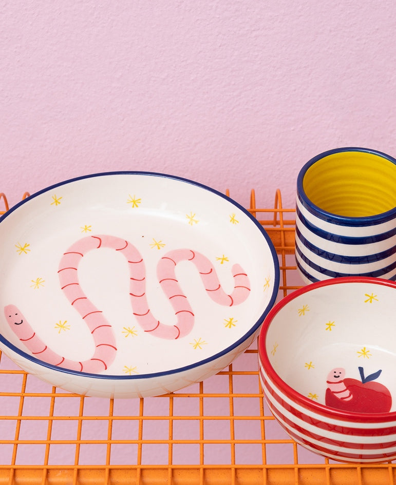 Drei farbenfrohe Keramikschüsseln auf einem orangefarbenen Gitter, verziert mit Motiven von Würmern und Streifen.