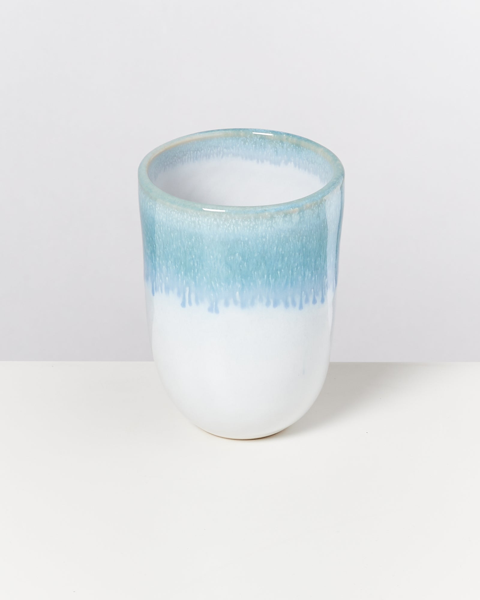 Weiße Keramiktasse mit hellblauem Rand auf weißem Hintergrund.