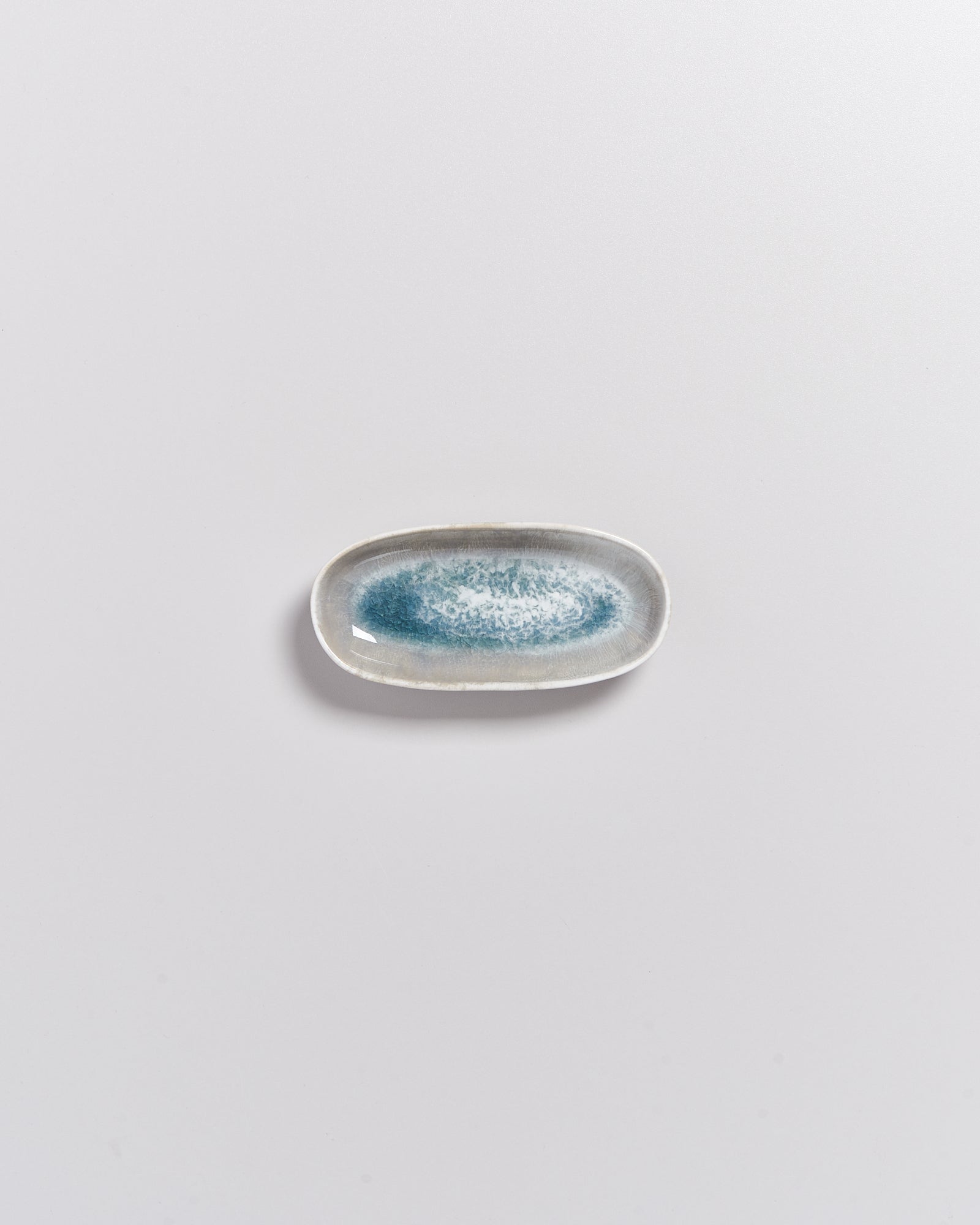 Kleiner, ovaler Teller mit blau-weißer Glasur auf grauem Hintergrund.