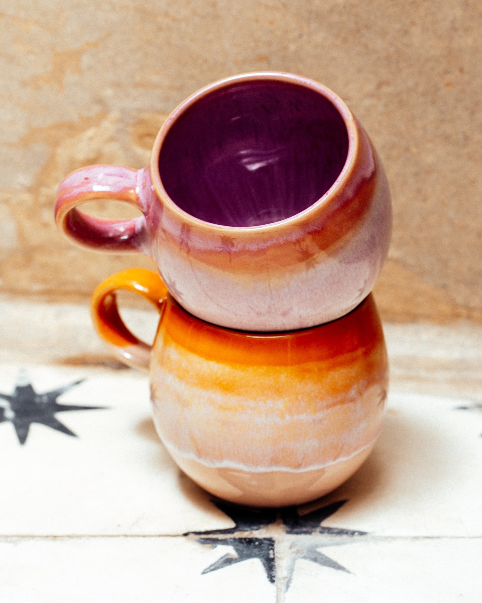 Zwei bunte Keramiktassen stapeln sich auf einem Fliesenboden mit Sternenmotiv.