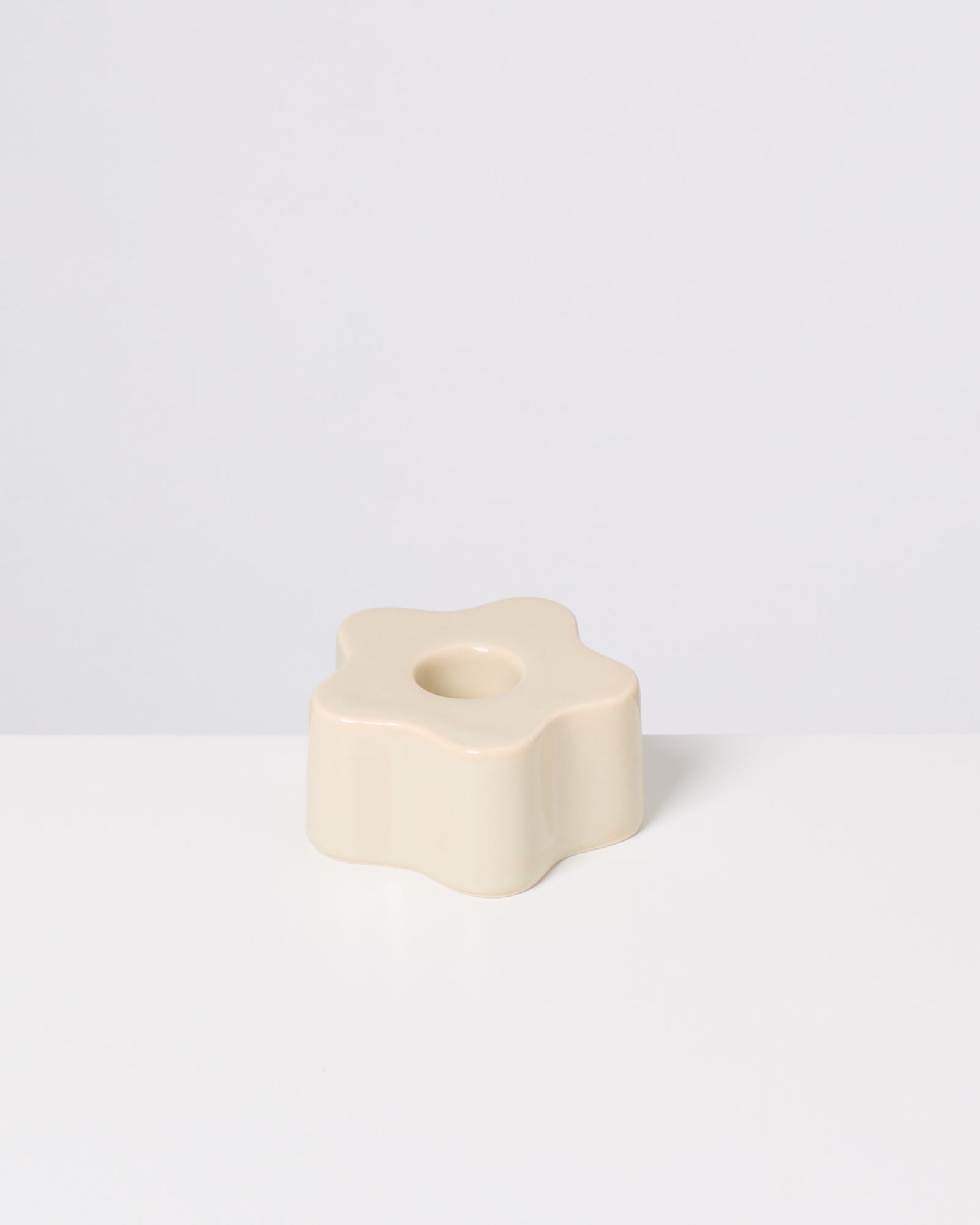 Beigefarbene, blumenförmige Kerzenhalterung mit rundem Loch, auf weißem Hintergrund.