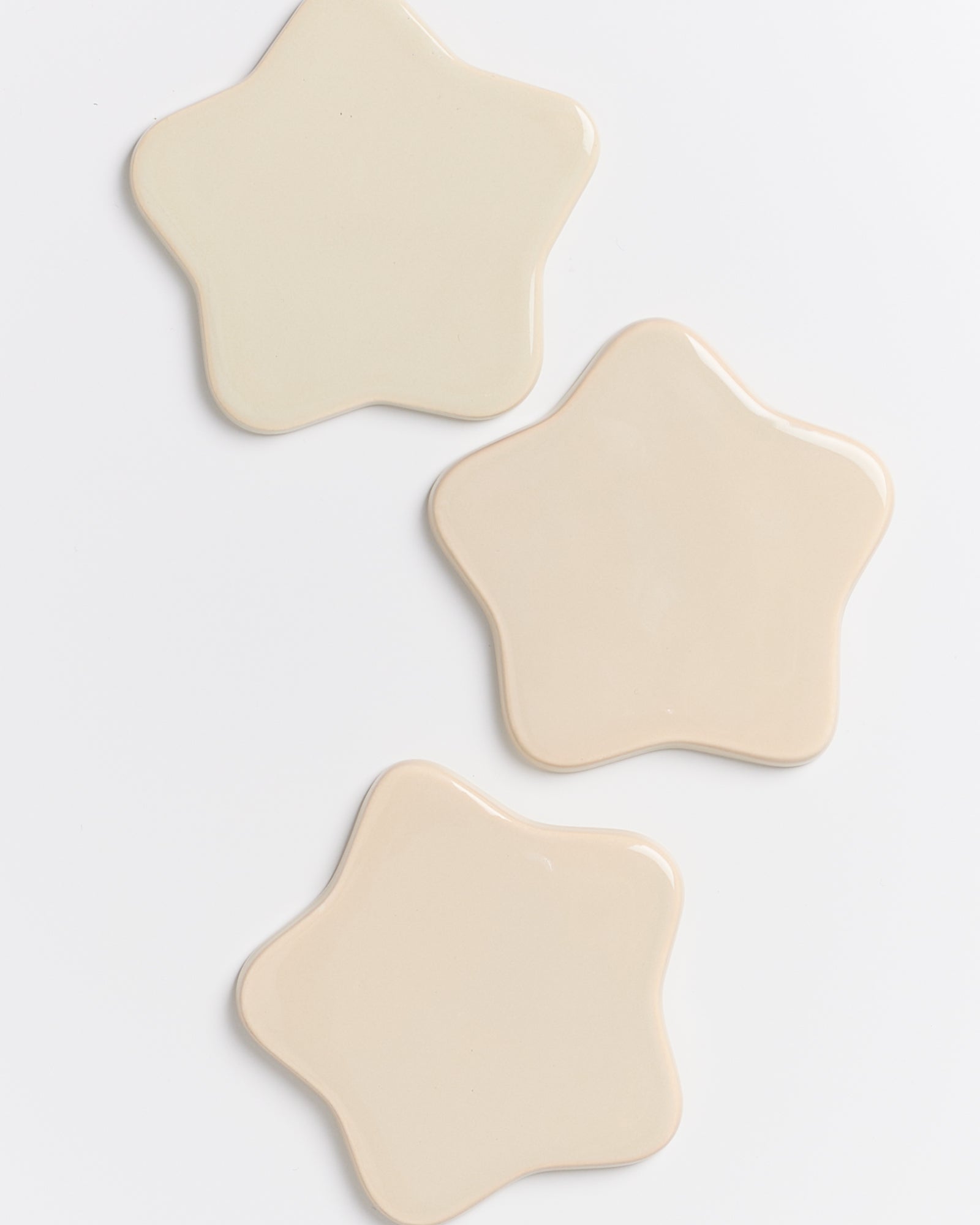 Drei sternförmige, beige Keramikkacheln liegen auf einem weißen Hintergrund.