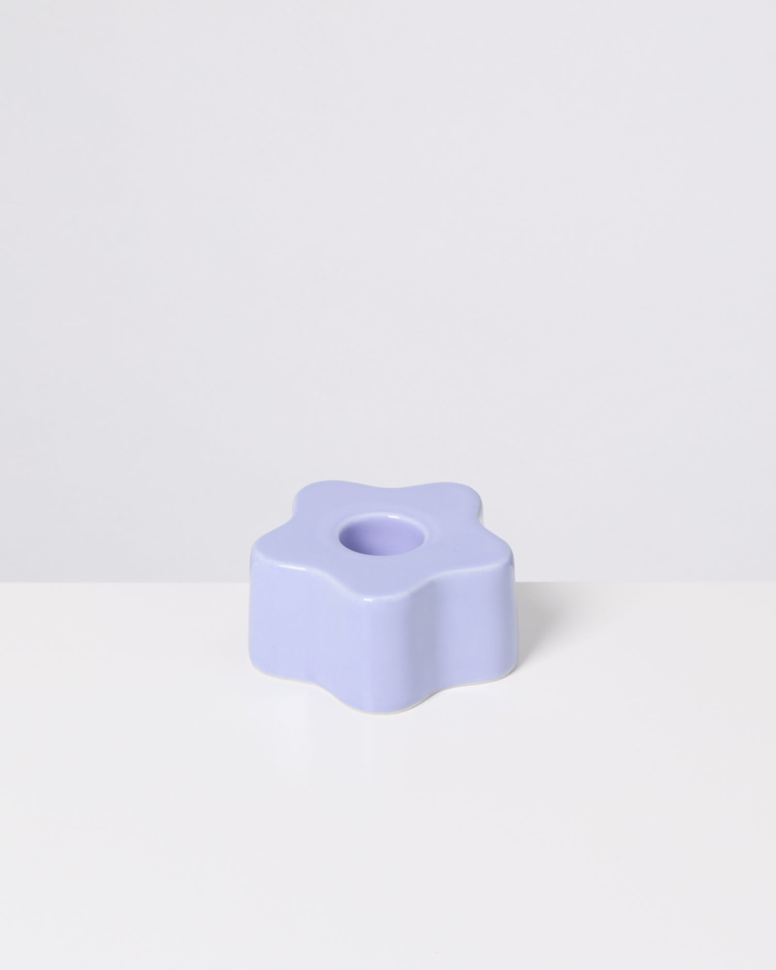 Lila, sternförmiger Kerzenhalter aus Keramik auf einer weißen Oberfläche.