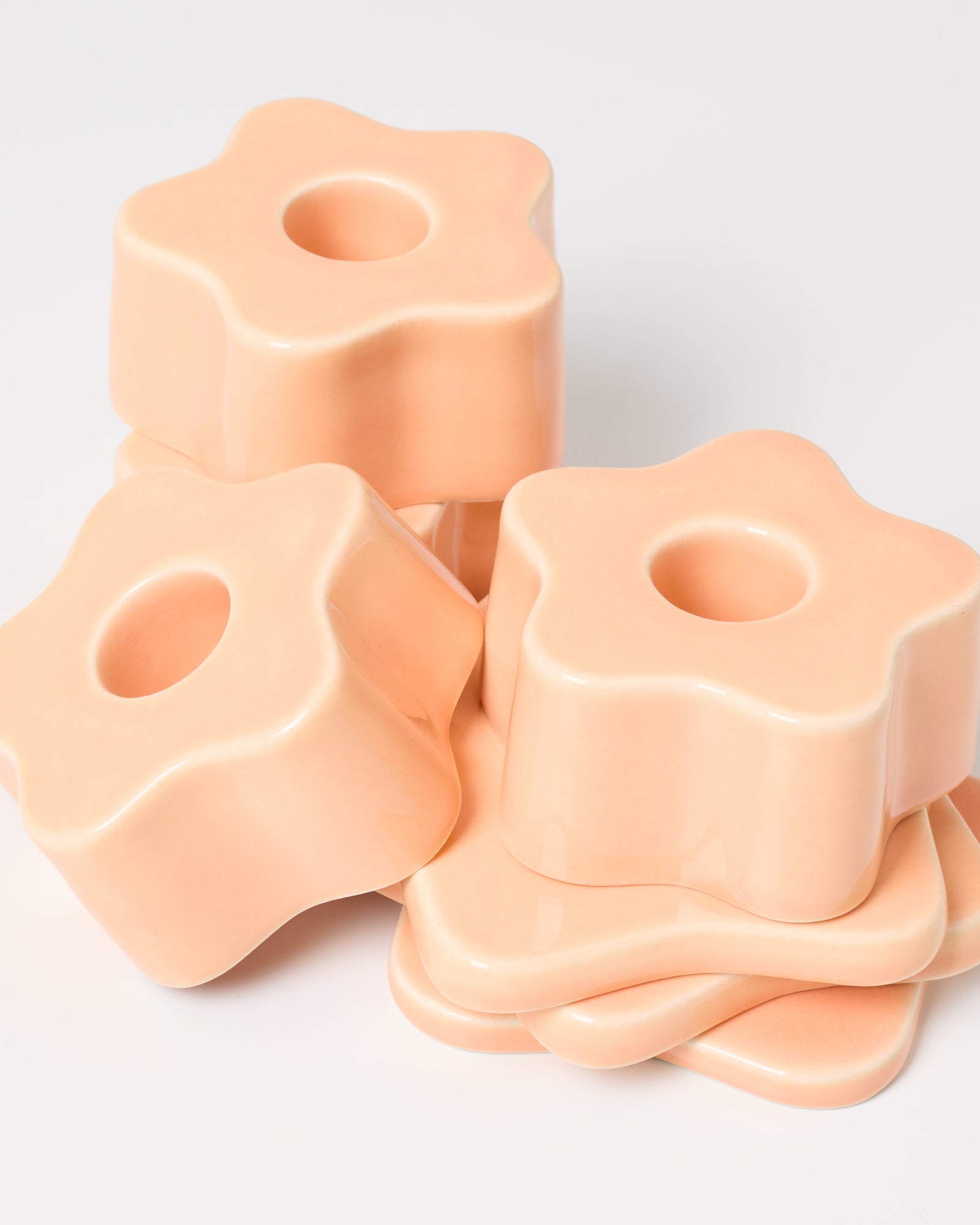 Stapel rosafarbener, blumenähnlicher Keramikformen mit zentrierten Löchern auf weißem Hintergrund.