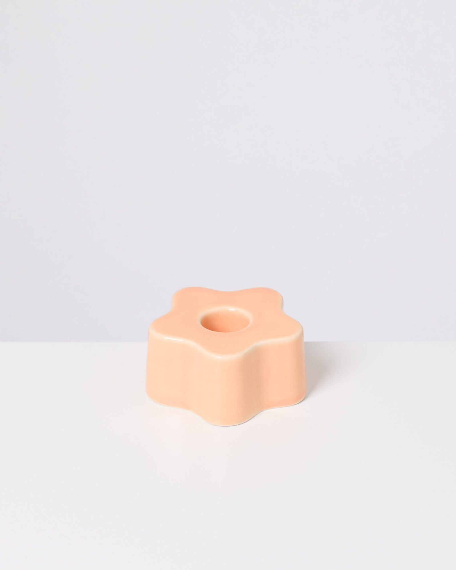 Pfirsichfarbener, blumenförmiger Kerzenhalter mit Loch in der Mitte auf einem weißen Hintergrund.