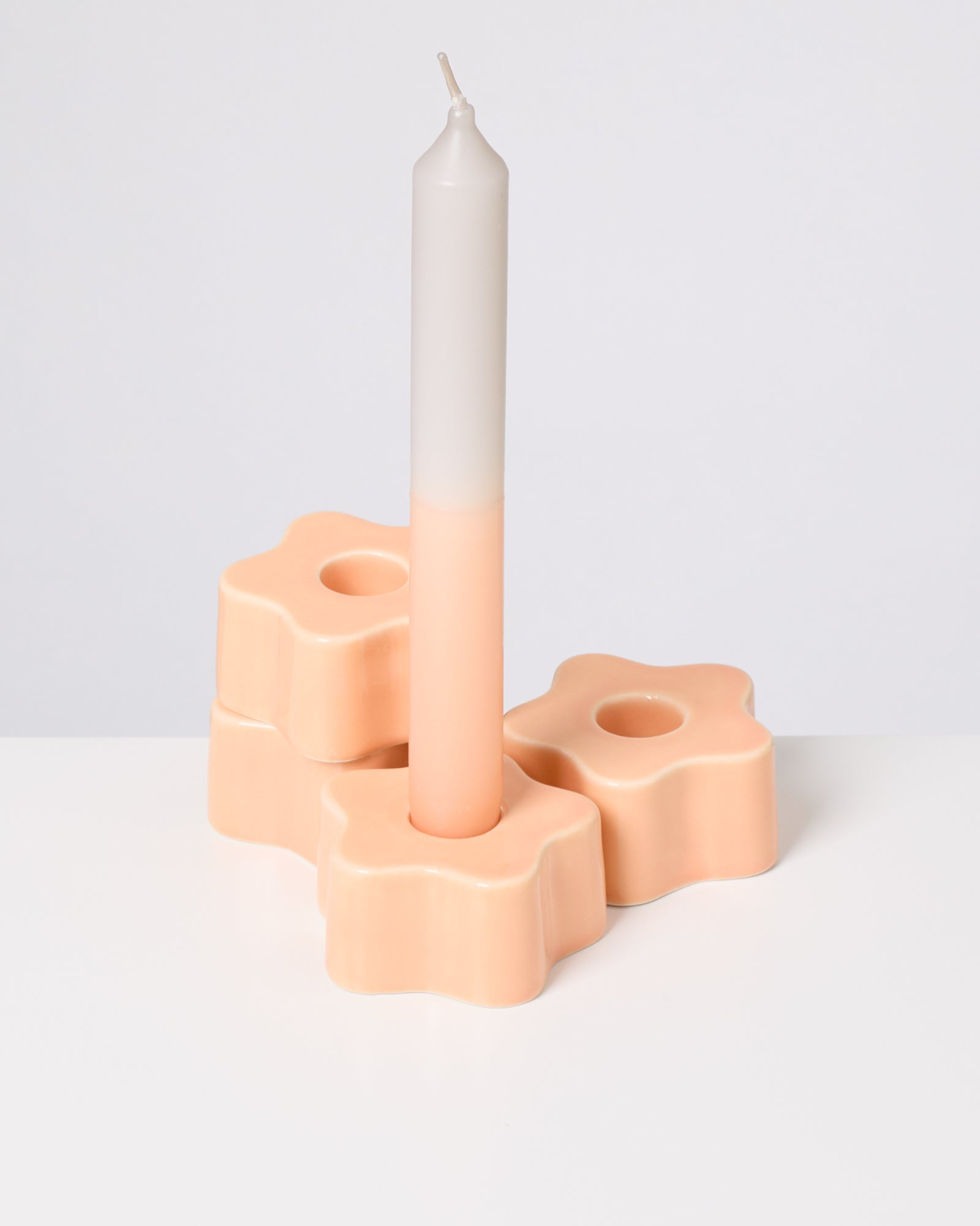 Kerze in einem pfirsichfarbenen, blumenförmigen Kerzenhalter auf weißem Hintergrund.
