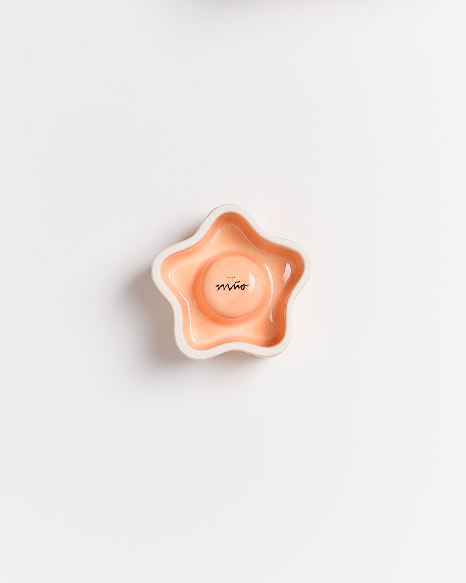 Sternförmige, orange Schale mit glasiertem Innenraum und der Aufschrift „Miro“ auf einem weißen Hintergrund.