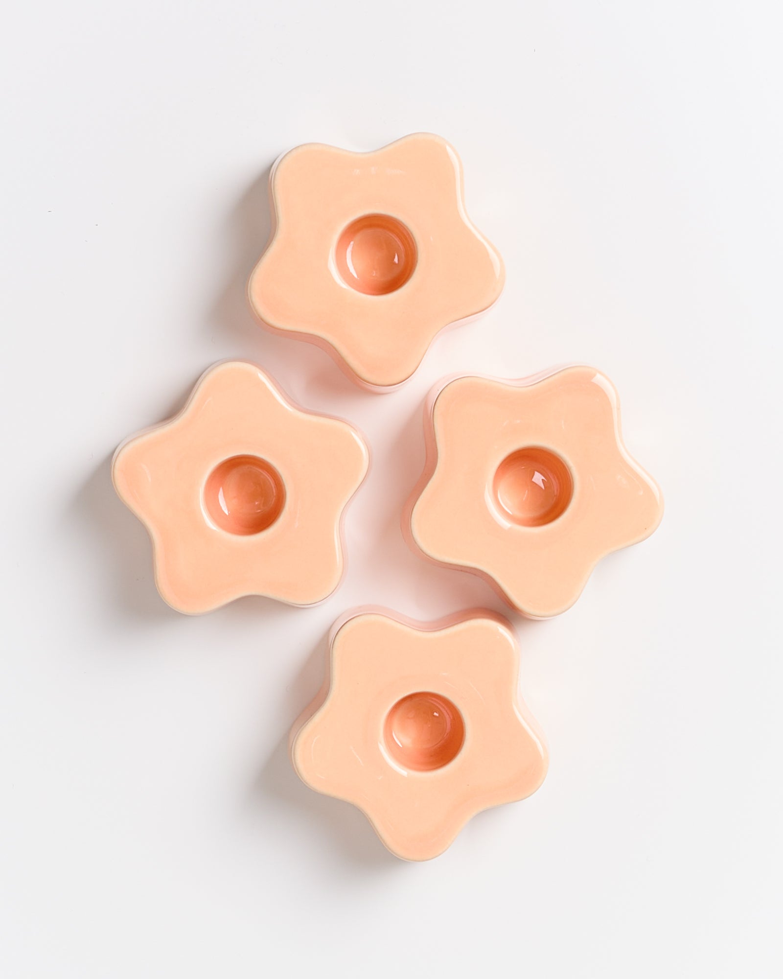 Vier orange, blumenförmige Keramikformen auf weißem Hintergrund.