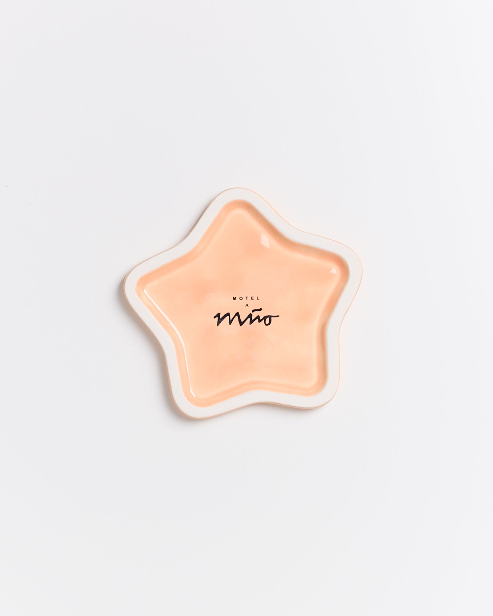 Sternförmiger, orangefarbener Teller mit dem Aufdruck "Motel a Miio" in einem minimalistischen Design auf weißem Hintergrund.
