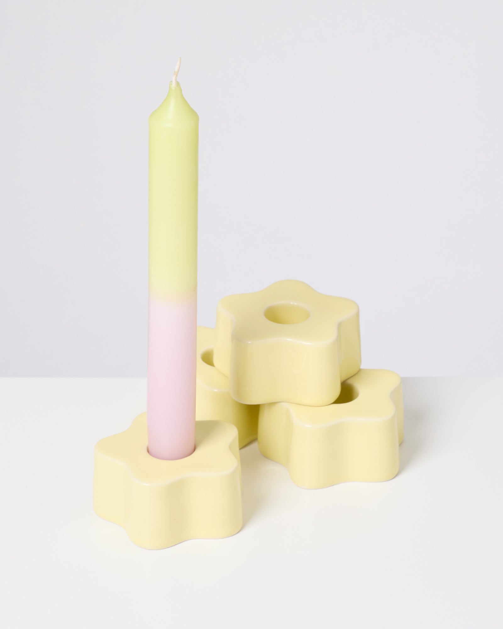 Eine zweifarbige Kerze in einem blütenförmigen, gelben Kerzenhalter vor einem weißen Hintergrund.