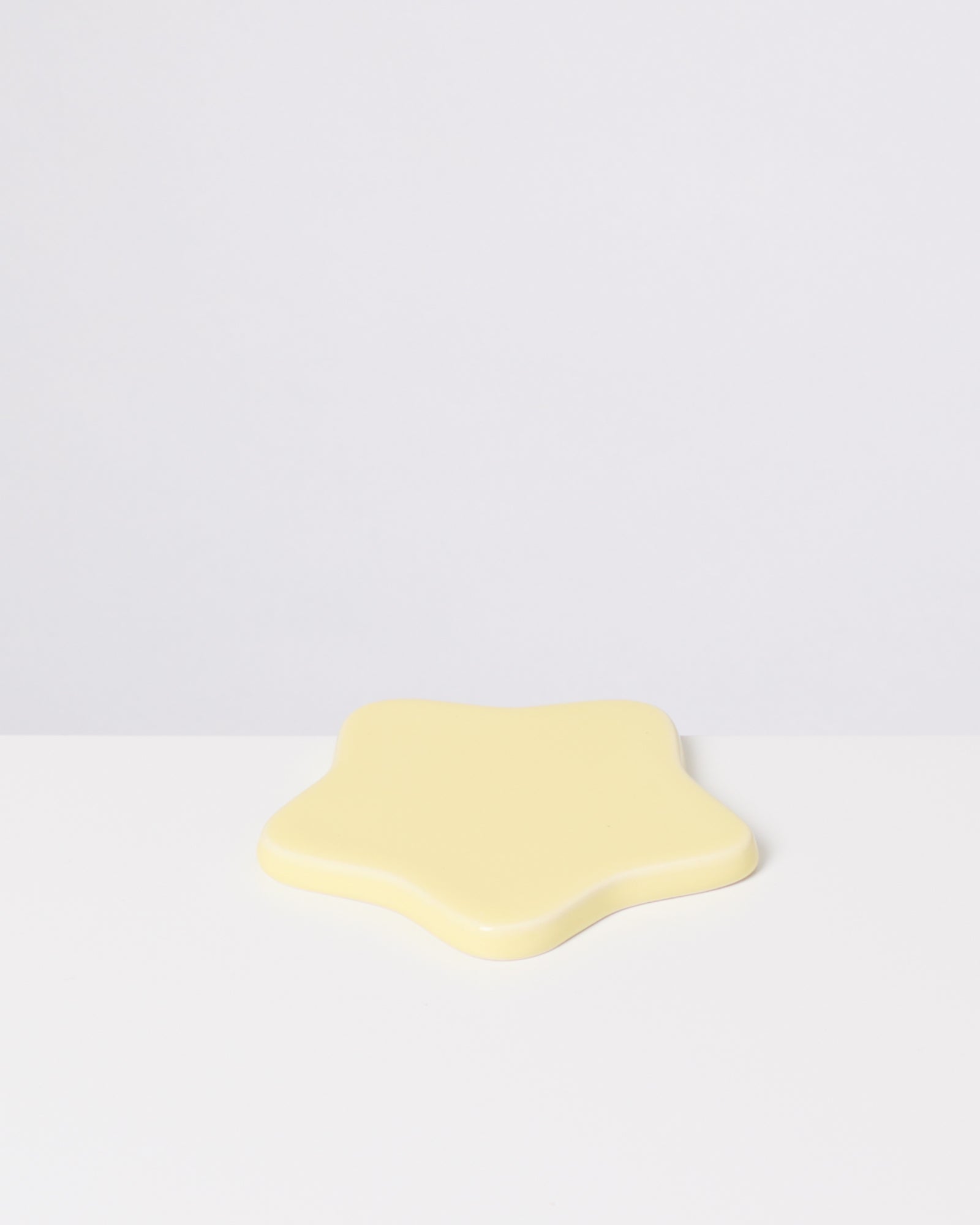 Gelber, sternförmiger Gegenstand auf einer weißen Oberfläche vor grauem Hintergrund.