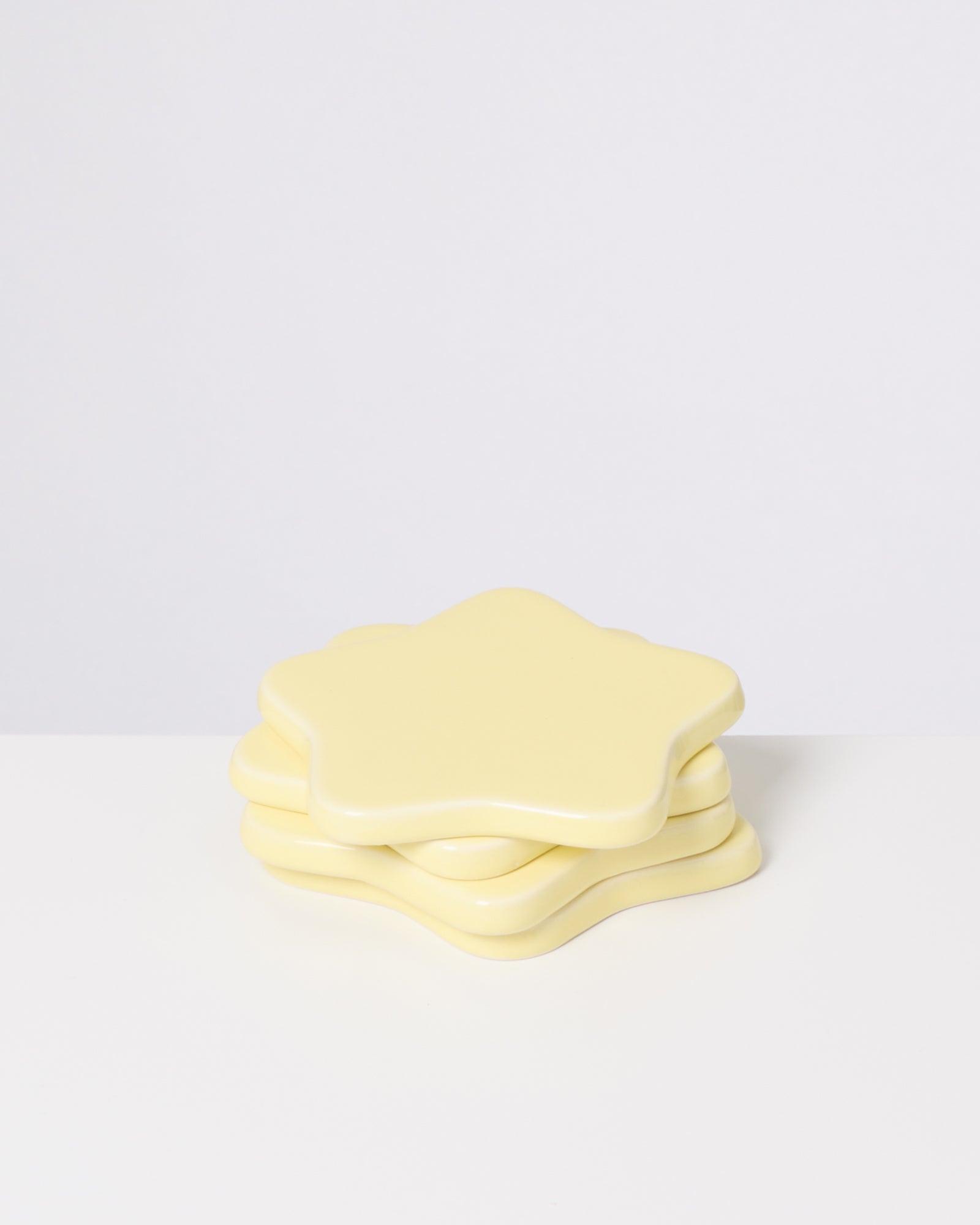 Drei hellgelbe, sternförmige Untersetzer sind auf einem weißen Tisch übereinander gestapelt.