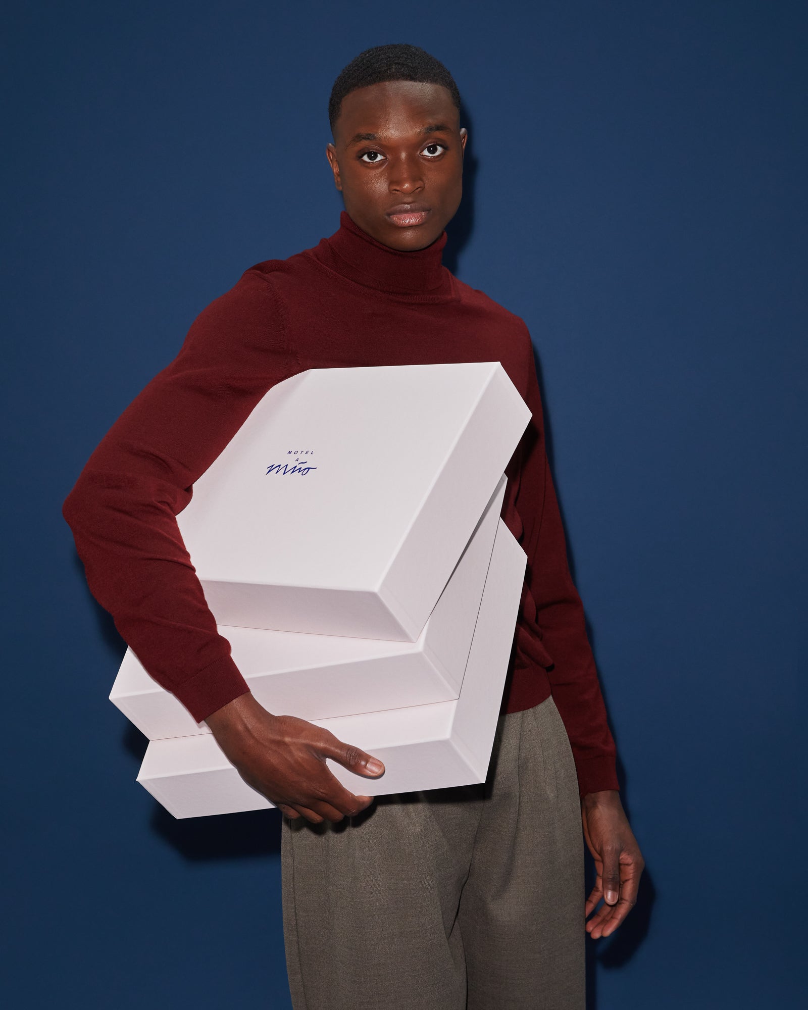 Person in einem roten Pullover hält drei weiße Schachteln vor einem dunkelblauen Hintergrund.