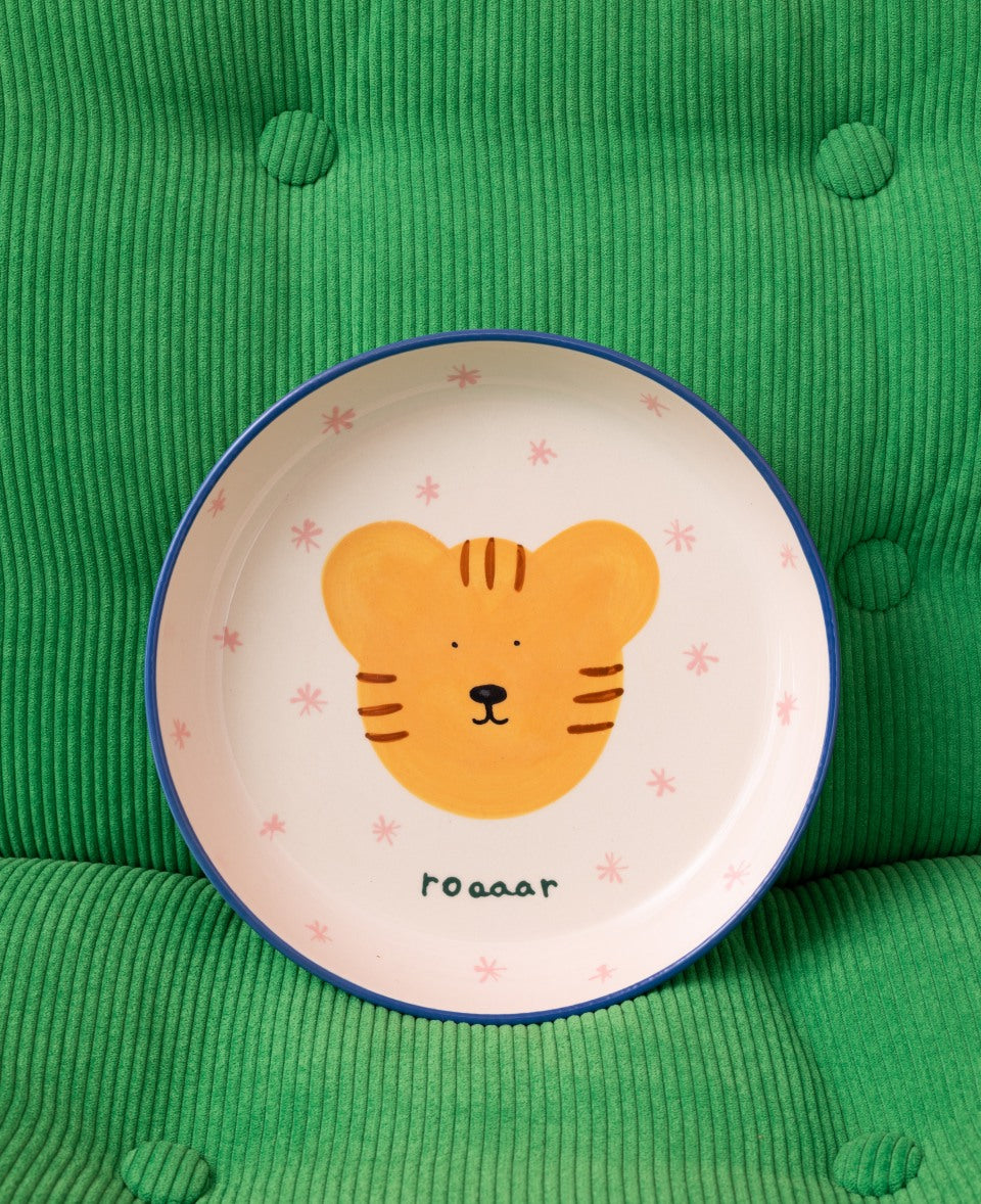 Ein Teller mit einer gelben Tierzeichnung und dem Wort "roaaar" liegt auf einem grünen, gesteppten Stoff.