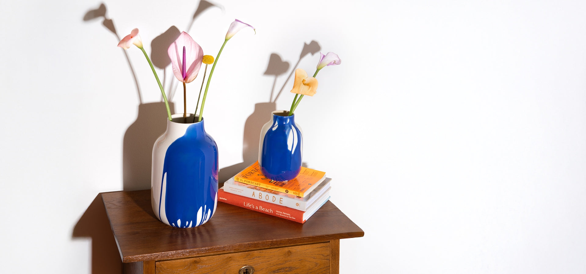 Zwei blaue Vasen mit Blumen stehen auf einem Holztisch; eine Vase steht auf Büchern.
