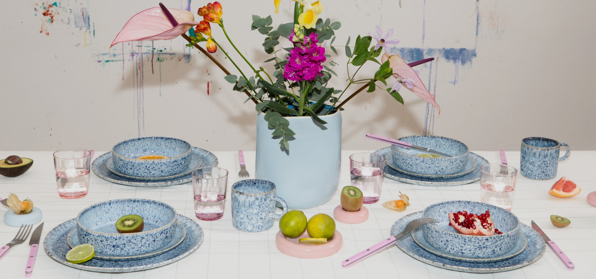 Gedeckter Tisch mit blauem Geschirr, Gläsern, exotischen Früchten und Blumen in einer blauen Vase.