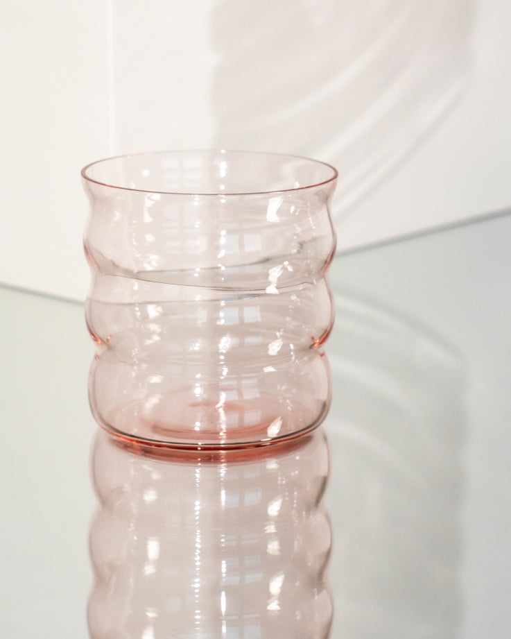 Ein geriffeltes, transparentes Glas mit leicht rosa Tönung steht auf einem spiegelnden Untergrund.
