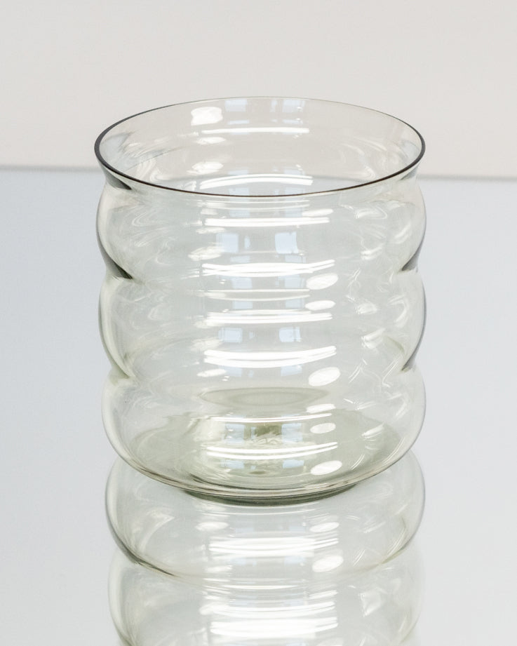 Gerippte, transparente Glasvase mit reflektierenden Lichtmustern auf einer glänzenden Oberfläche.