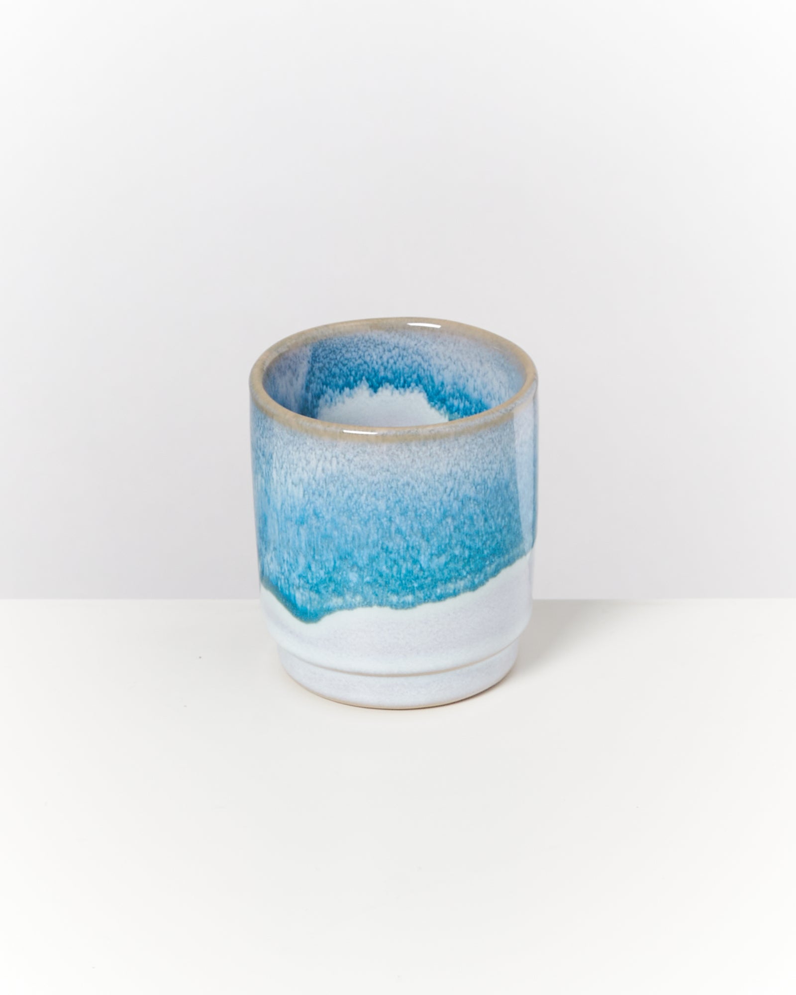 Blauer und weißer Keramikbecher mit sanftem Farbverlauf, auf einem weißen Hintergrund platziert.