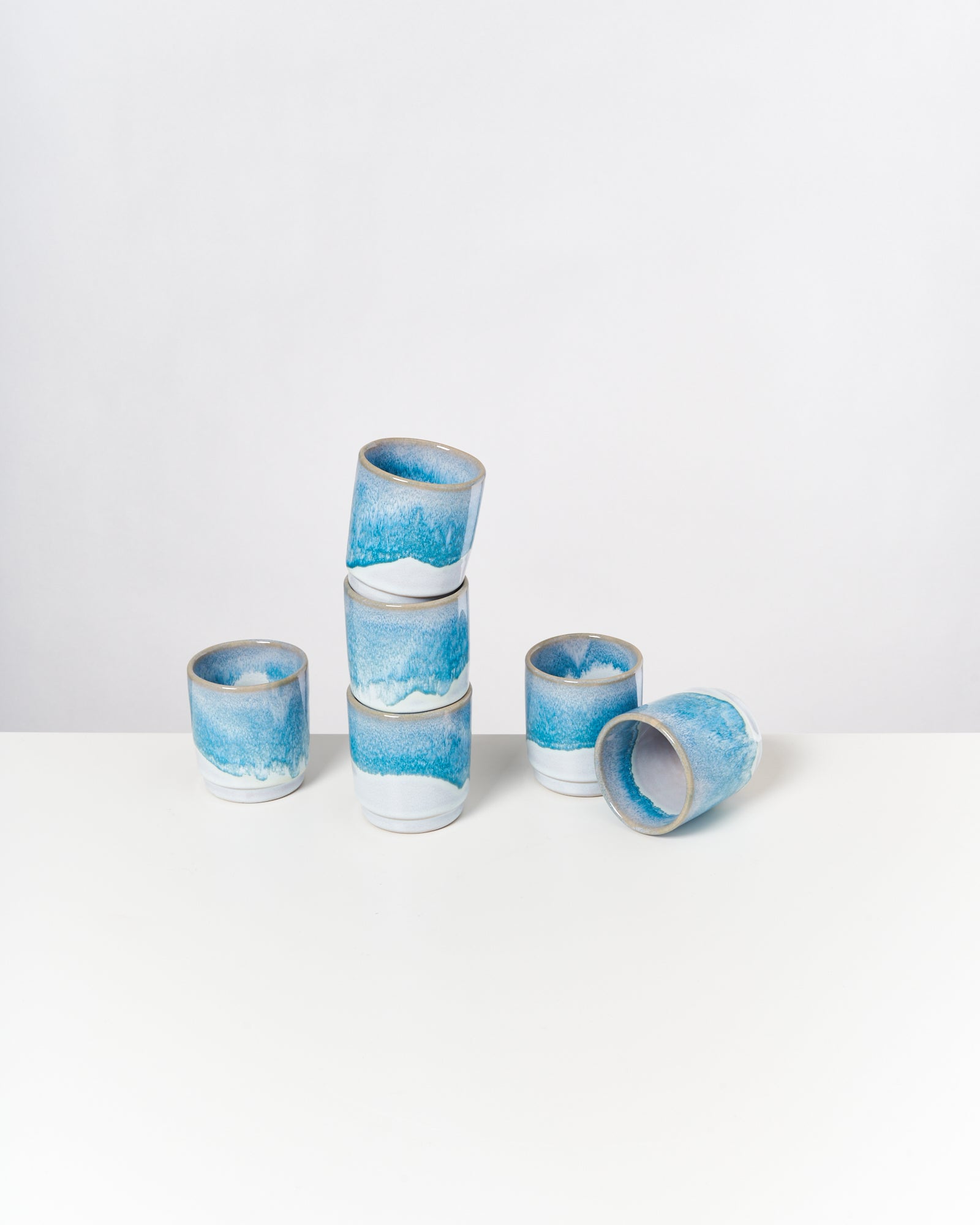 Sechs blau-weiße Keramikbecher, drei gestapelt, einer umgekippt, auf weißem Hintergrund.