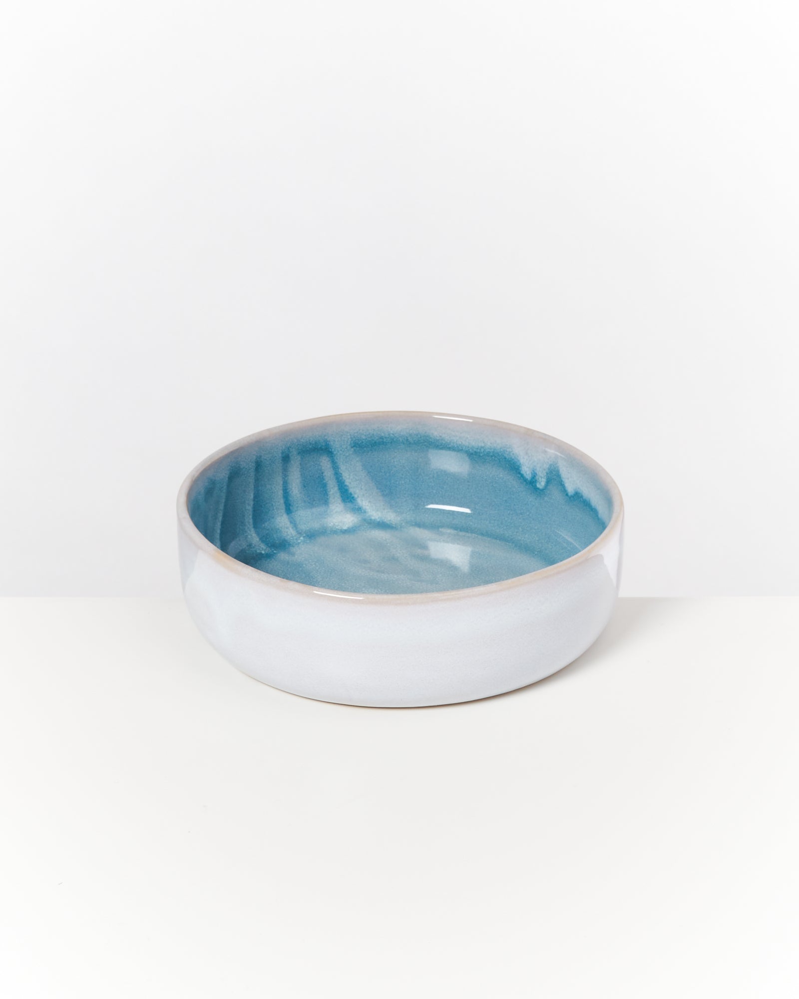 Keramikschüssel mit blauer Innenseite und weißer Außenseite, auf einer weißen Fläche platziert.