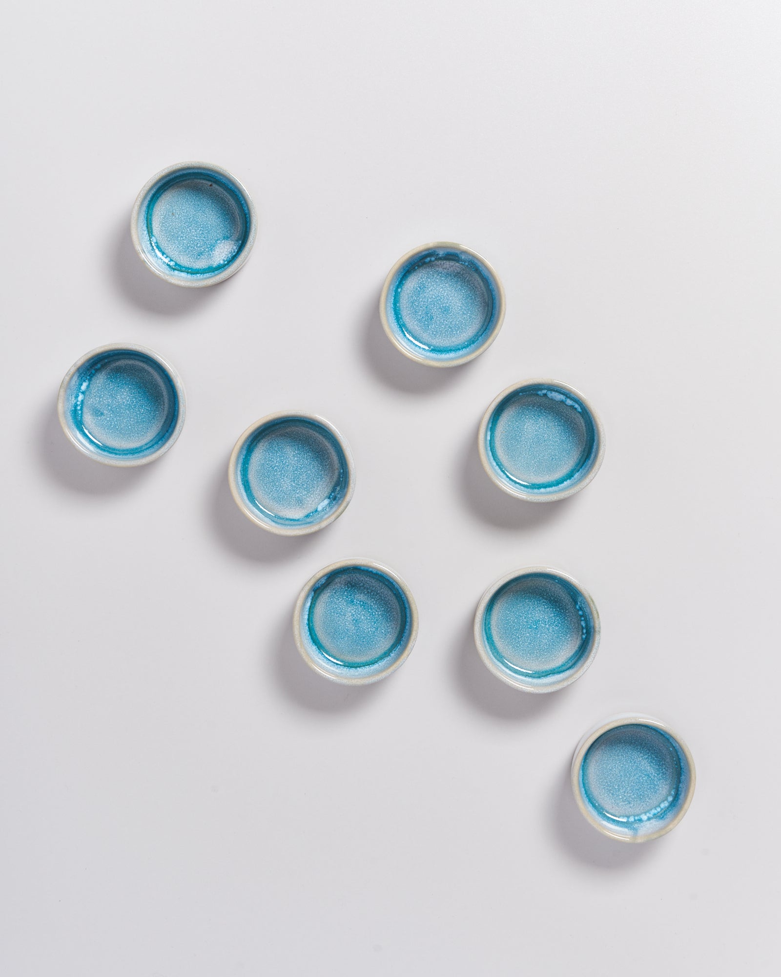 Acht kleine, runde Schalen mit blauer Glasur auf weißem Hintergrund.