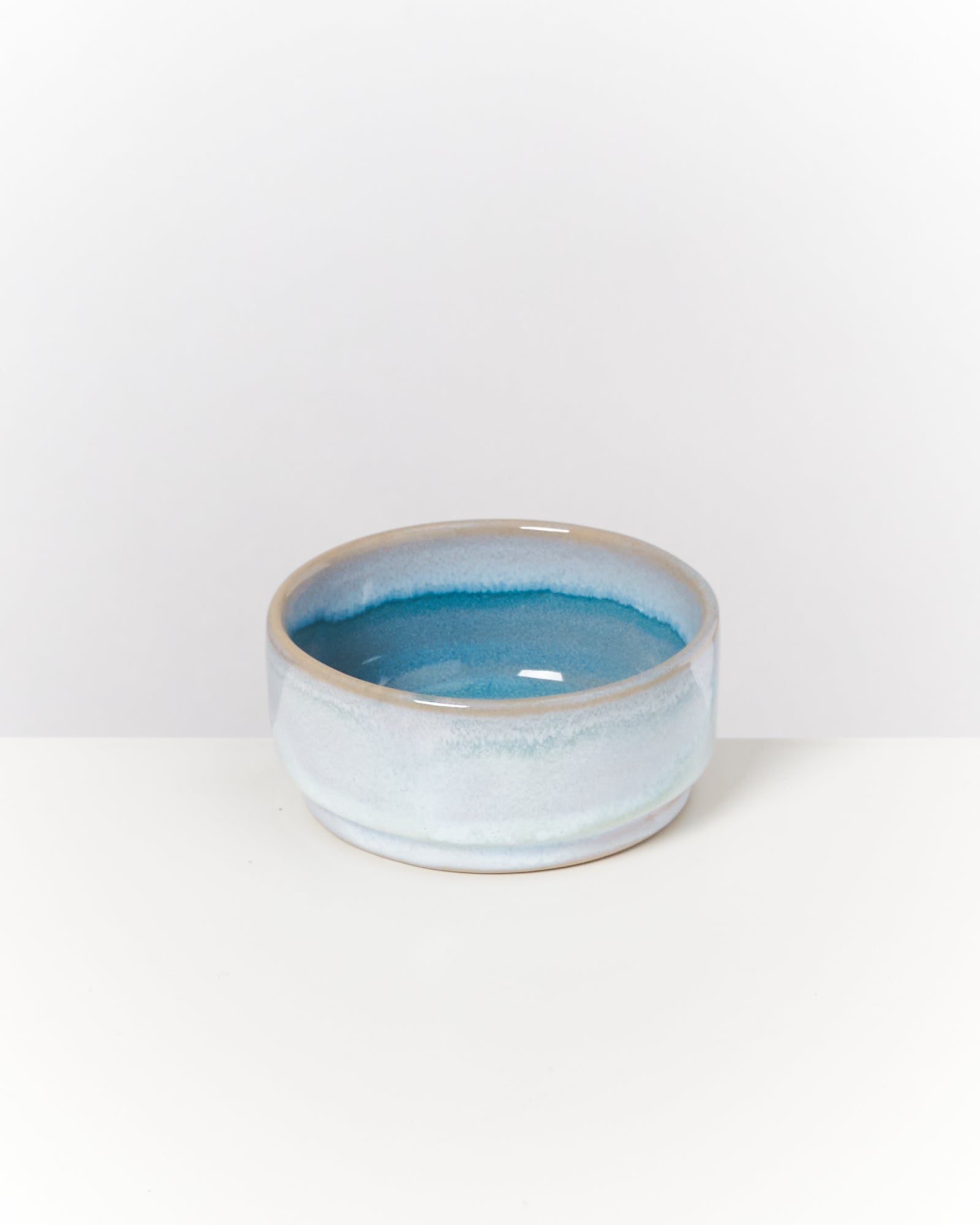 Eine flache, blau-weiß glasierte Keramikschale steht auf einer weißen Oberfläche.
