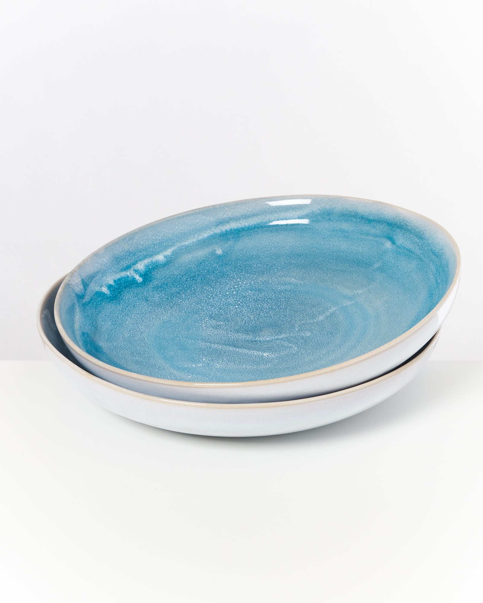 Zwei übereinander gestapelte, flache, blau glasierte Keramikteller auf einer weißen Oberfläche.