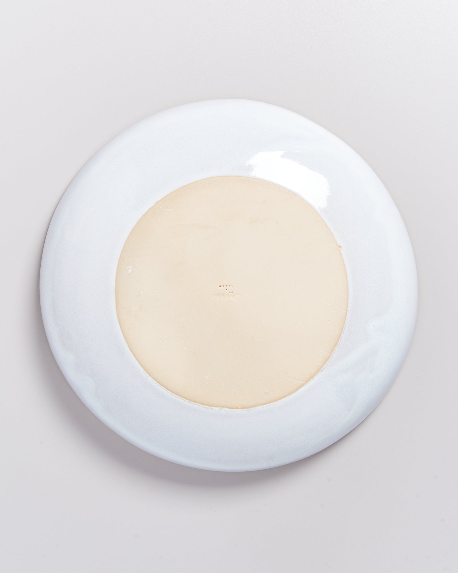 Rückseite eines runden Tellers mit cremefarbenem Zentrum und weißem Rand auf grauem Hintergrund.