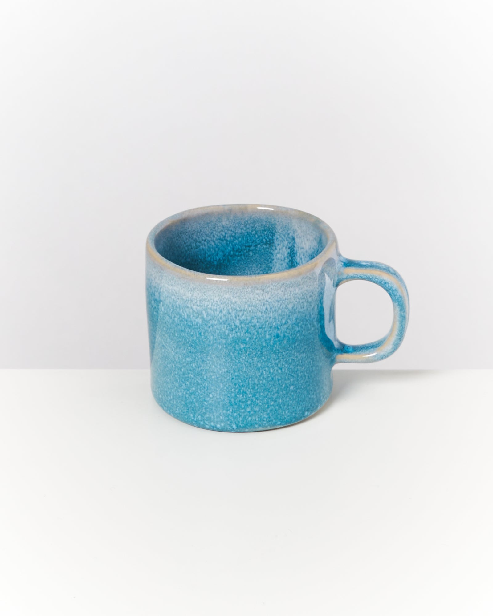 Blaue Keramiktasse mit Henkel auf weißem Hintergrund.