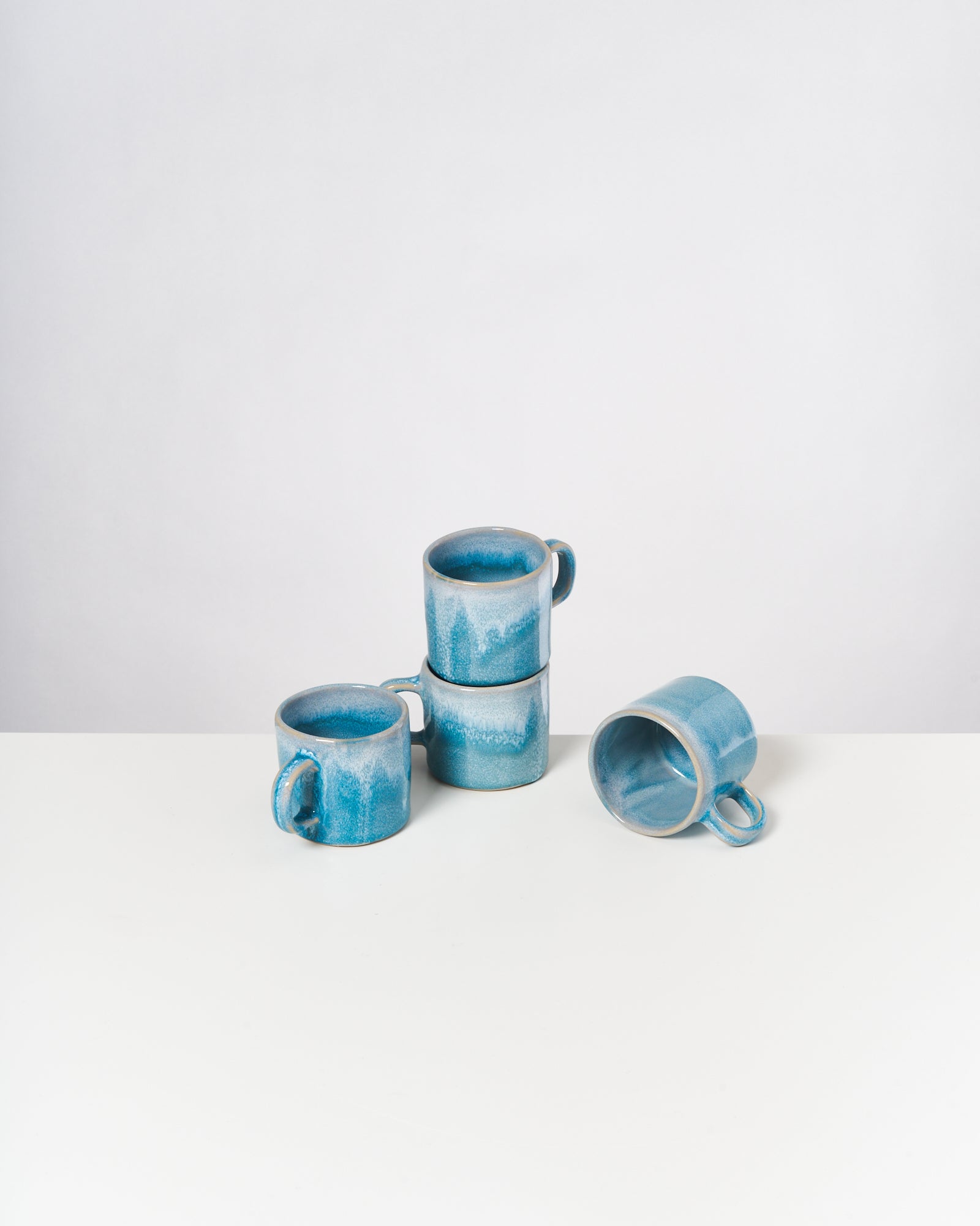 Vier blaue Keramiktassen, drei gestapelt und eine liegend, auf weißem Hintergrund.