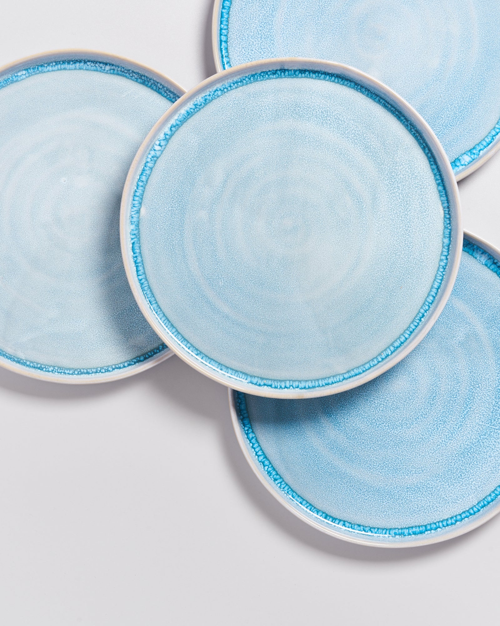 Vier blaue Keramikteller mit feinem Muster liegen überlappend auf einer weißen Oberfläche.