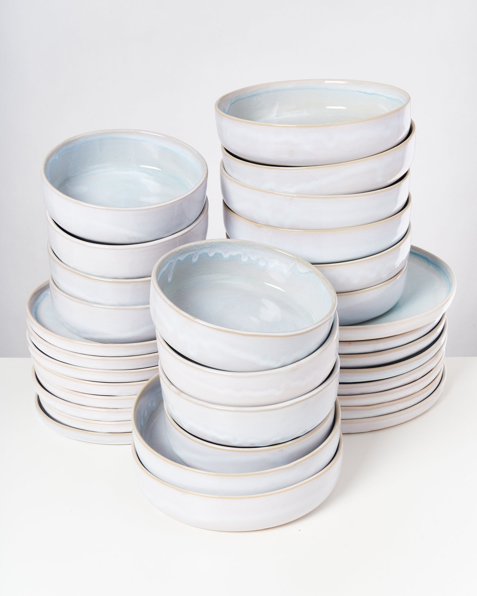Mehrere Stapel weißer, runder Keramikteller stehen auf einem weißen Untergrund.