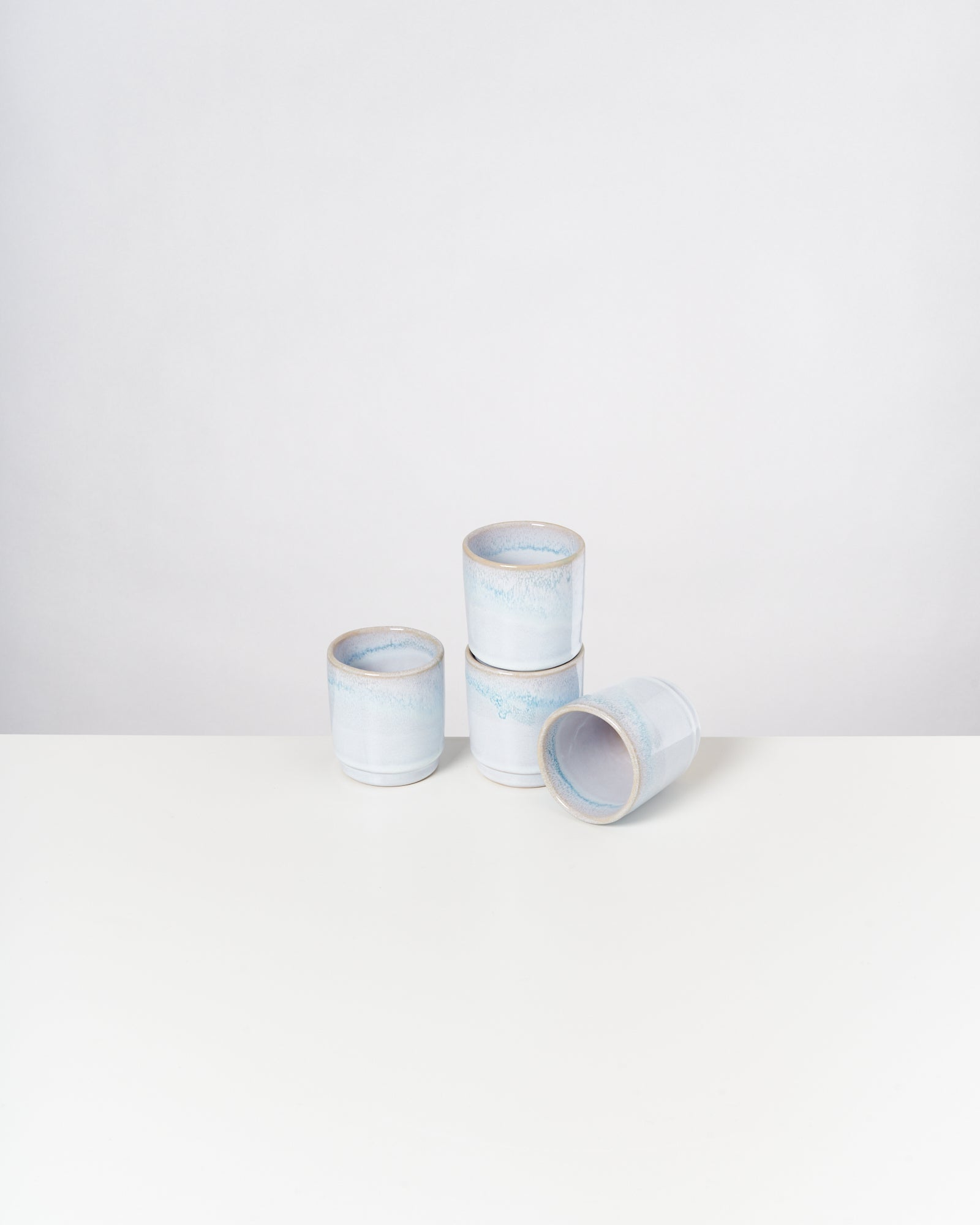 Vier stapelbare hellblaue Keramiktassen, drei aufeinander gestapelt, eine liegt seitlich auf einem weißen Tisch.