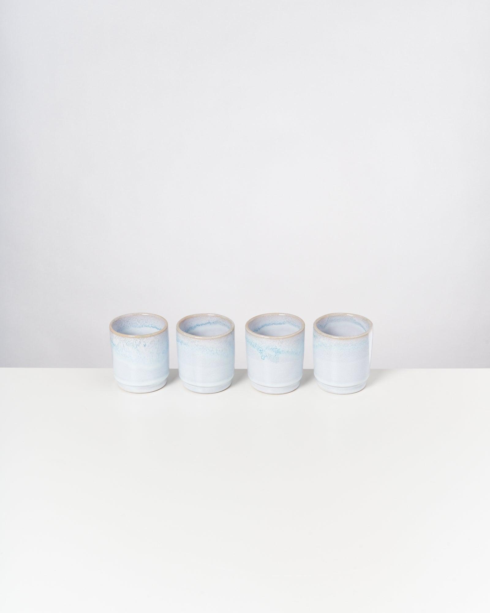 Vier hellblaue Keramiktassen stehen in einer Reihe auf einem weißen Tisch.