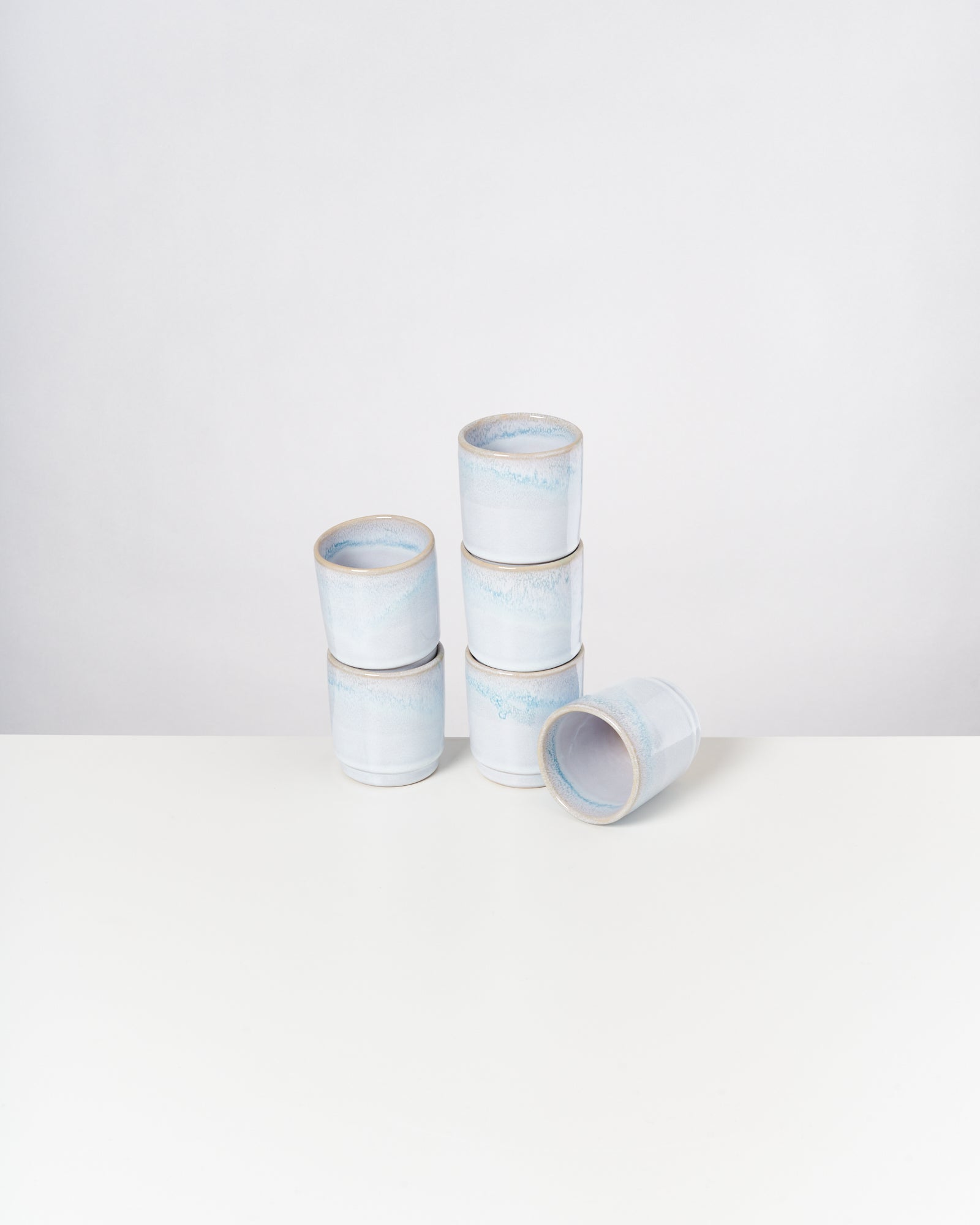 Sechs stapelbare, hellblaue Becher auf einem weißen Untergrund, einer liegt seitlich.