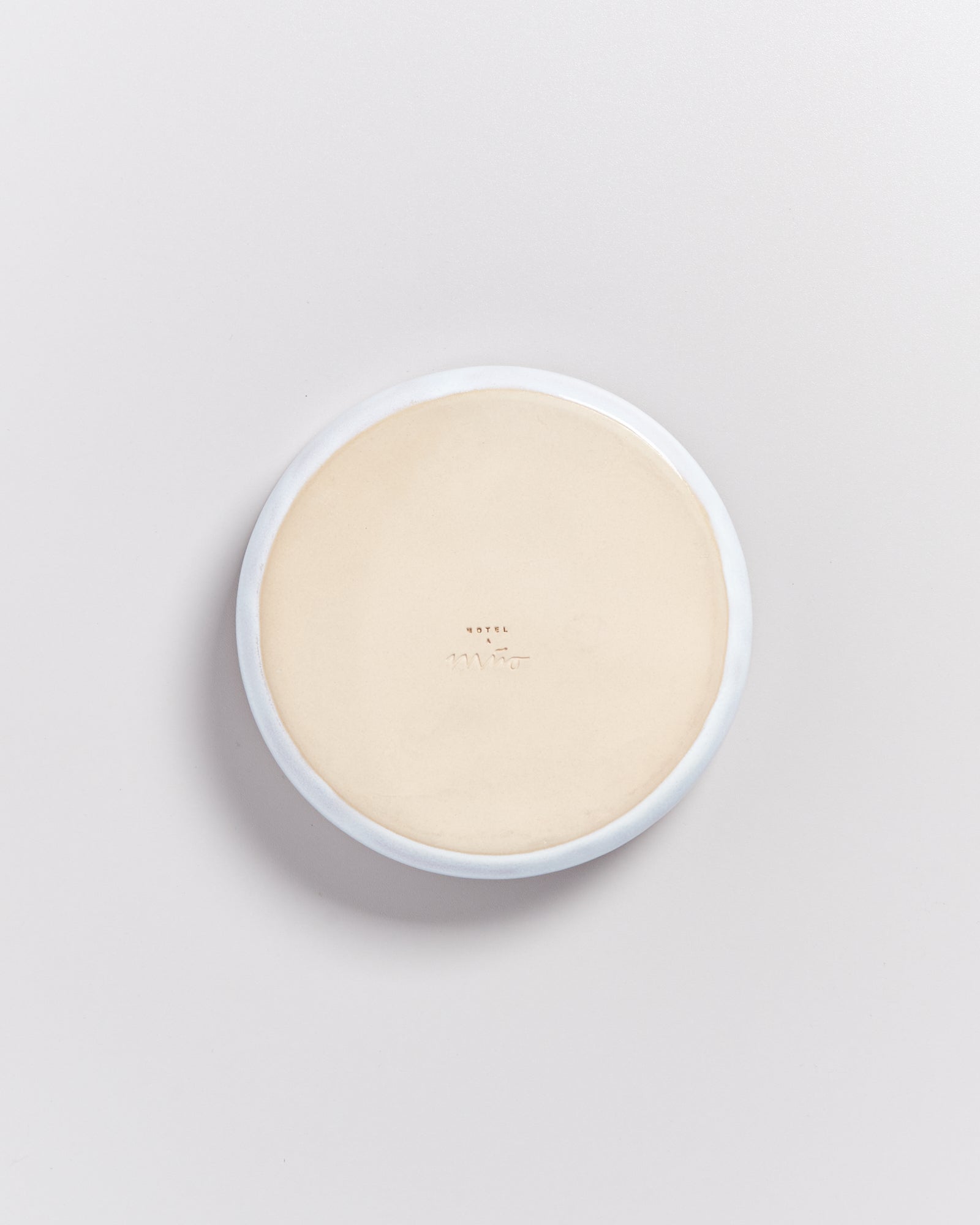 Runder, cremefarbener Untersetzer mit kleiner Prägung, auf weißem Hintergrund.