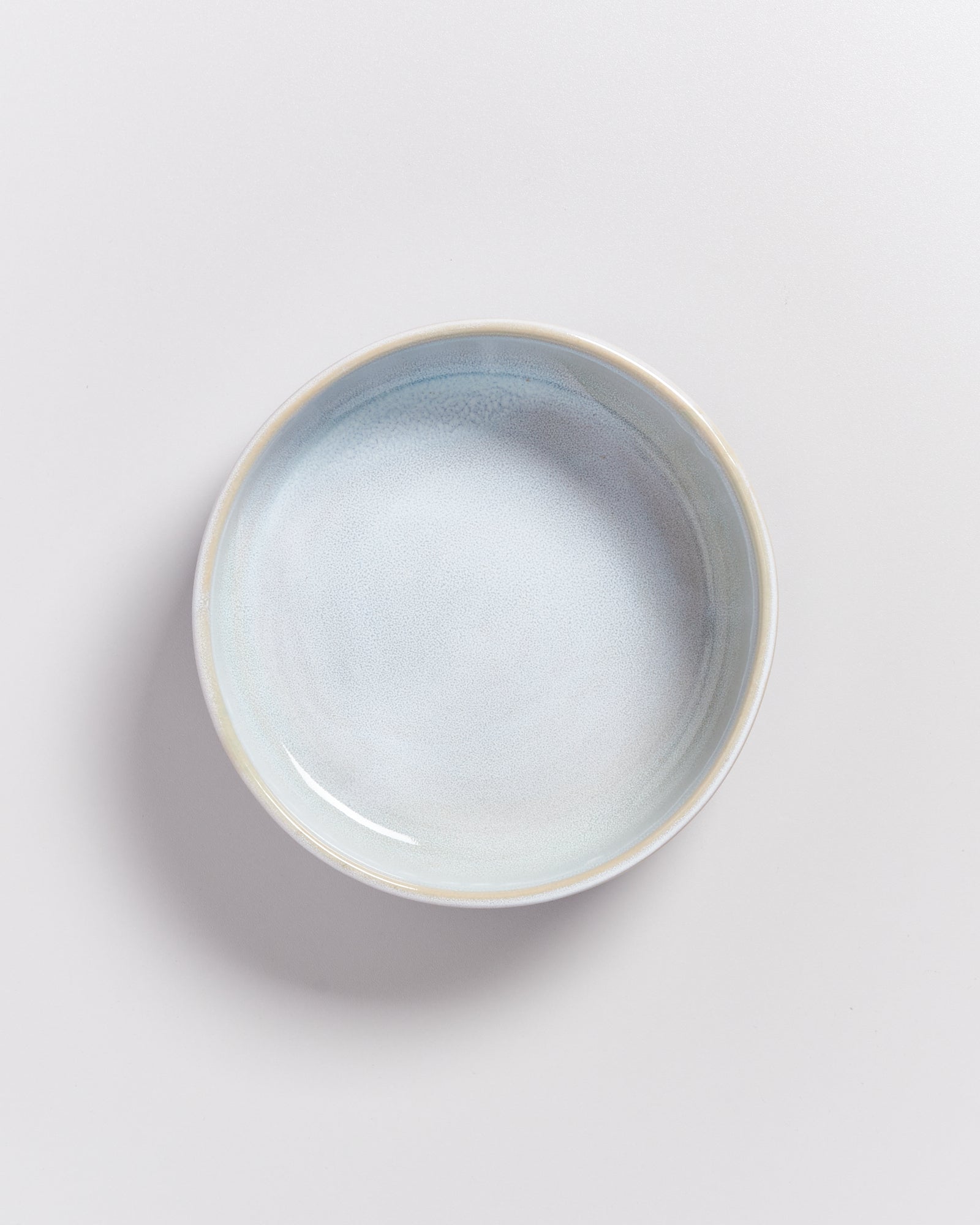 Eine leere, runde, hellblaue Keramikschale auf einem hellgrauen Hintergrund.