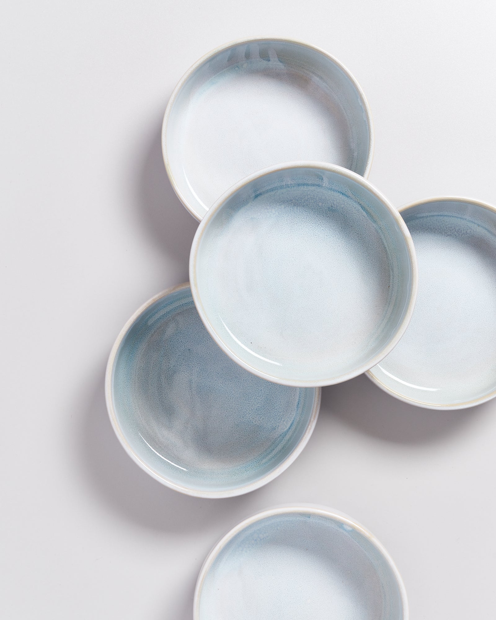 Fünf blaue Keramikteller sind elegant auf weißem Hintergrund angeordnet.