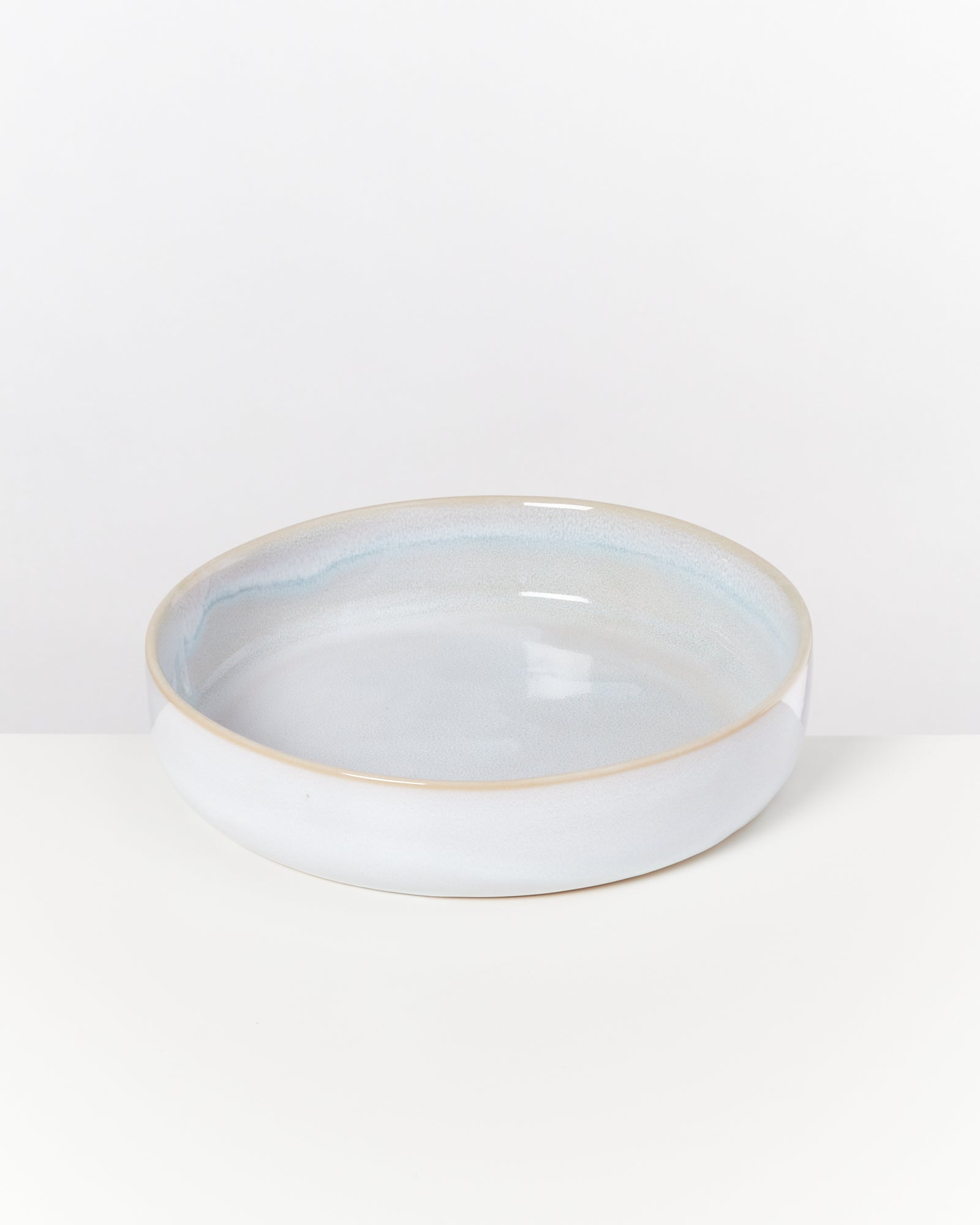 Weiße, runde Keramikschale mit einem zarten blauen Schimmer auf einem weißen Hintergrund.