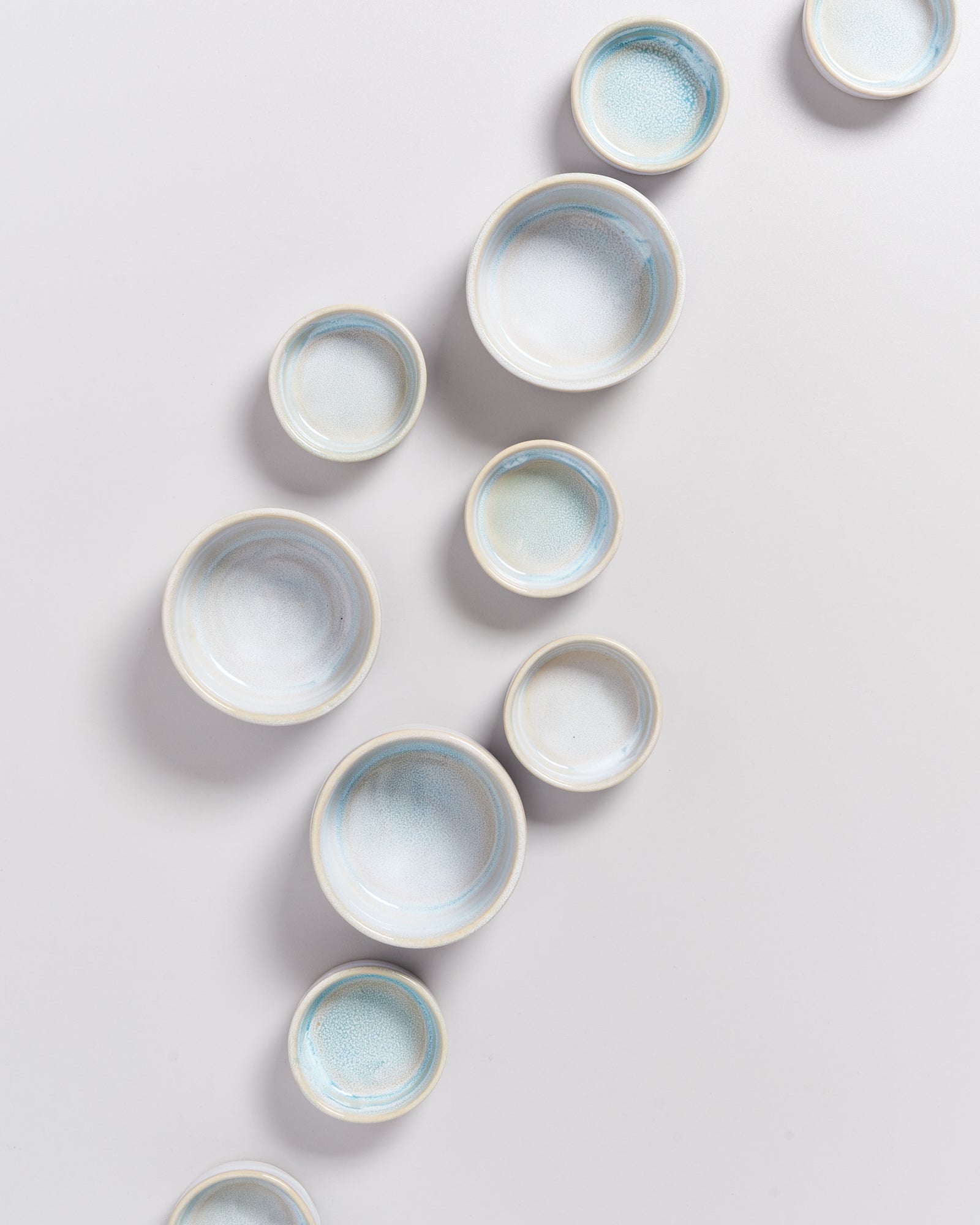 Mehrere Keramikschalen mit blau-weißer Glasur sind in diagonaler Anordnung auf einer weißen Oberfläche platziert.