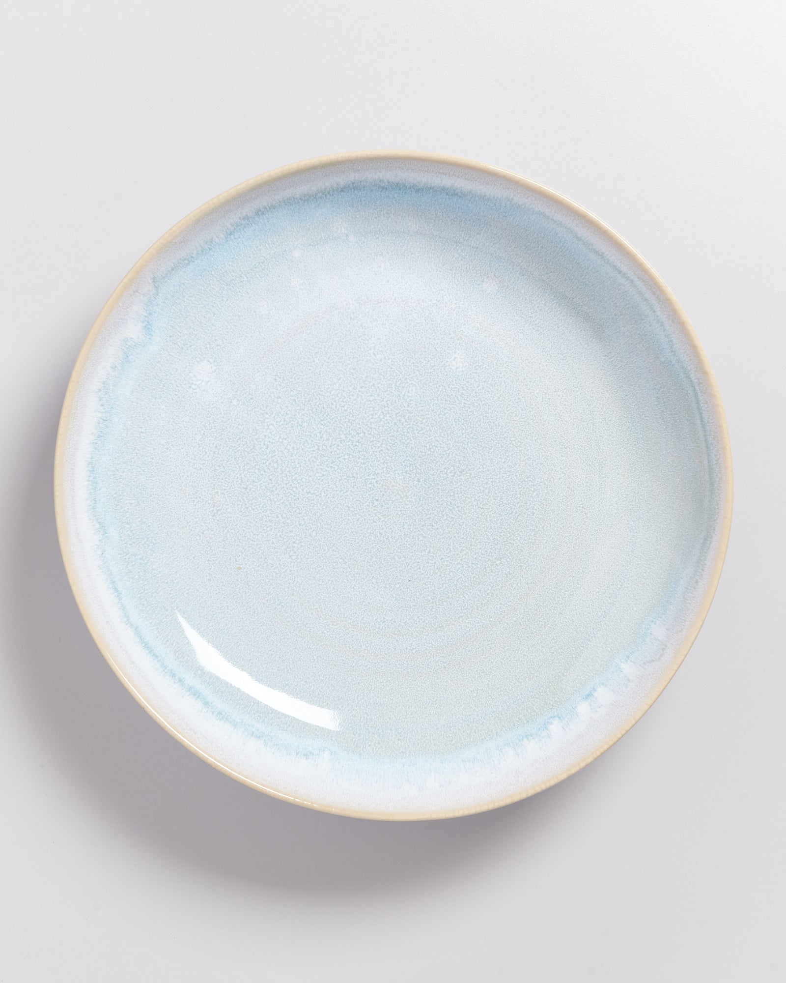 Ein heller Keramikteller mit bläulich-weißem Farbverlauf auf einer weißen Hintergrundfläche.