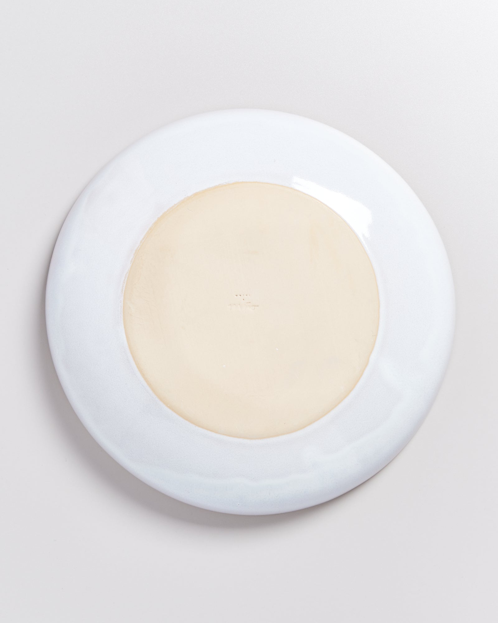 Unterseite eines weißen Tellers mit einem beige gefärbten inneren Kreis auf einem hellen Hintergrund.