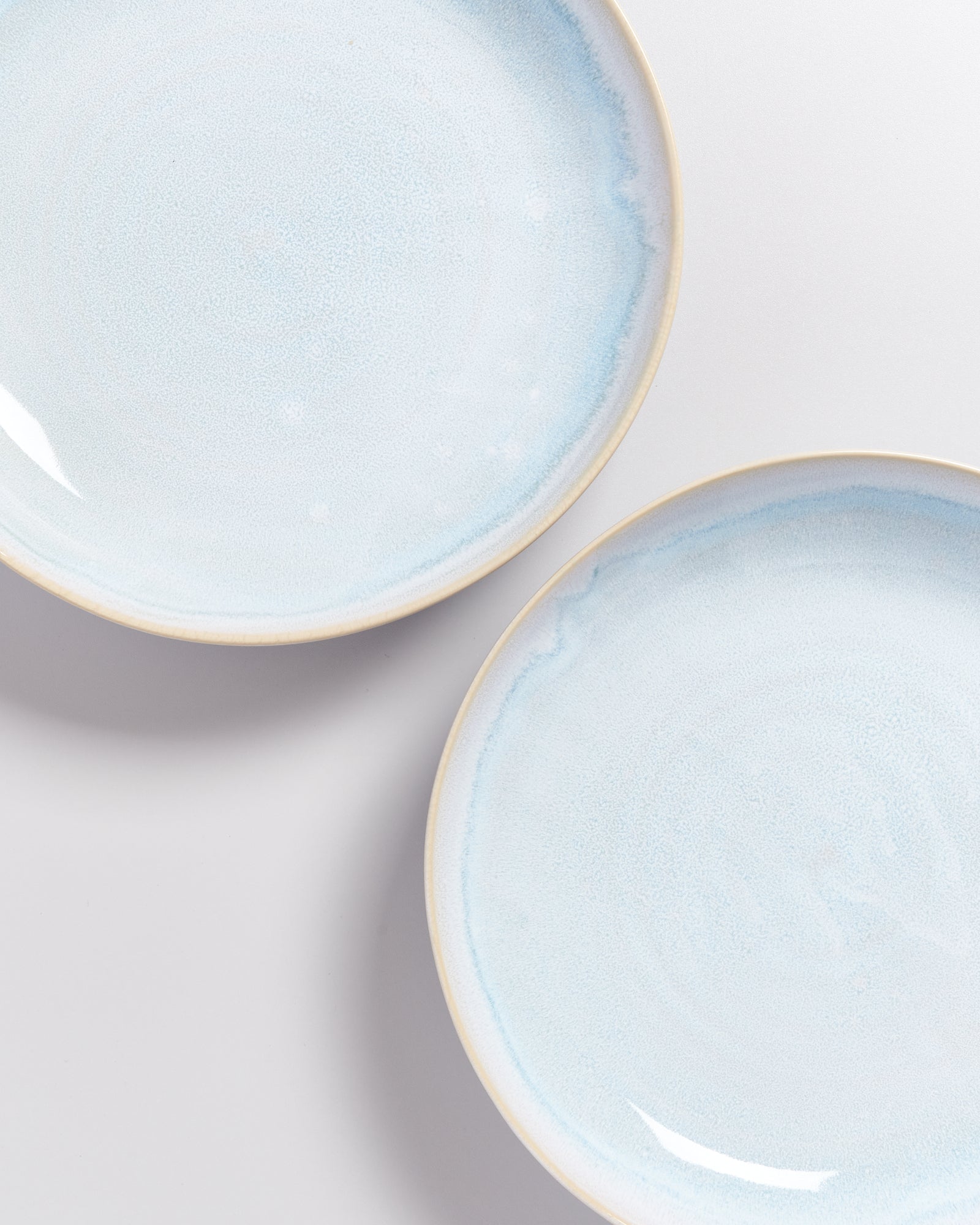 Zwei glatte, blaue Keramikteller auf weißem Hintergrund, leicht schräg angeordnet.