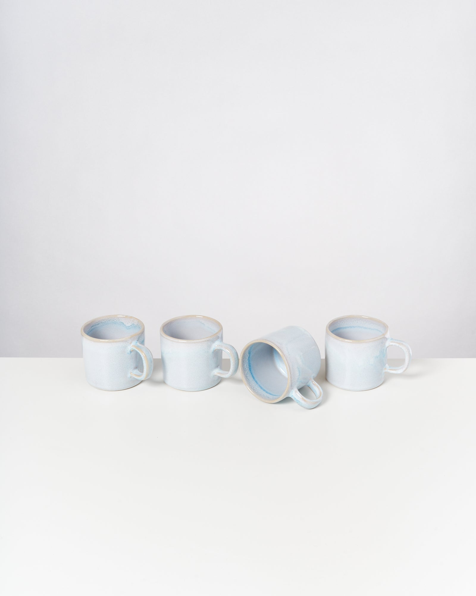Vier hellblaue Tassen auf einem weißen Tisch, eine davon liegt seitlich.